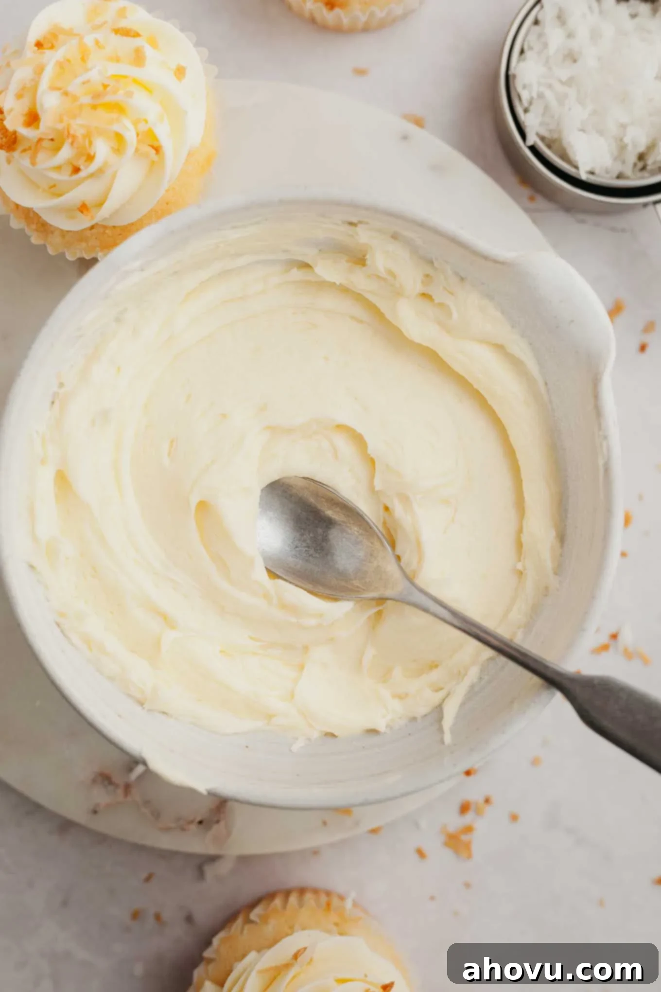 A close-up shot of a bowl brimming with creamy coconut frosting, with a spoon gently resting in it, inviting a taste.