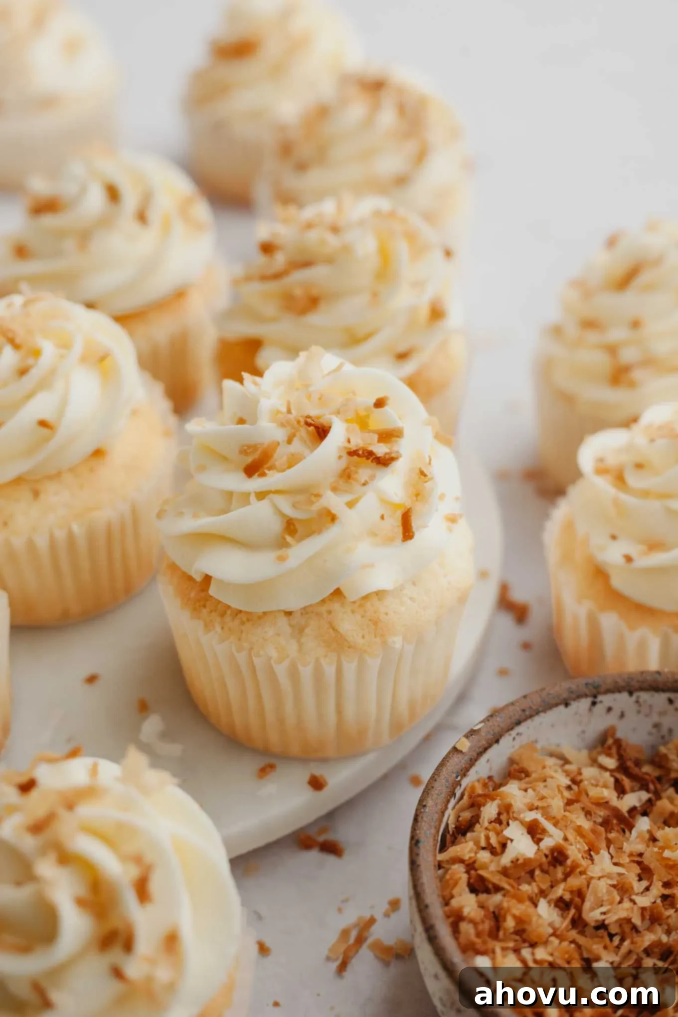 Several coconut cupcakes beautifully topped with creamy coconut frosting and garnished with delicate toasted coconut flakes for added flavor and texture.