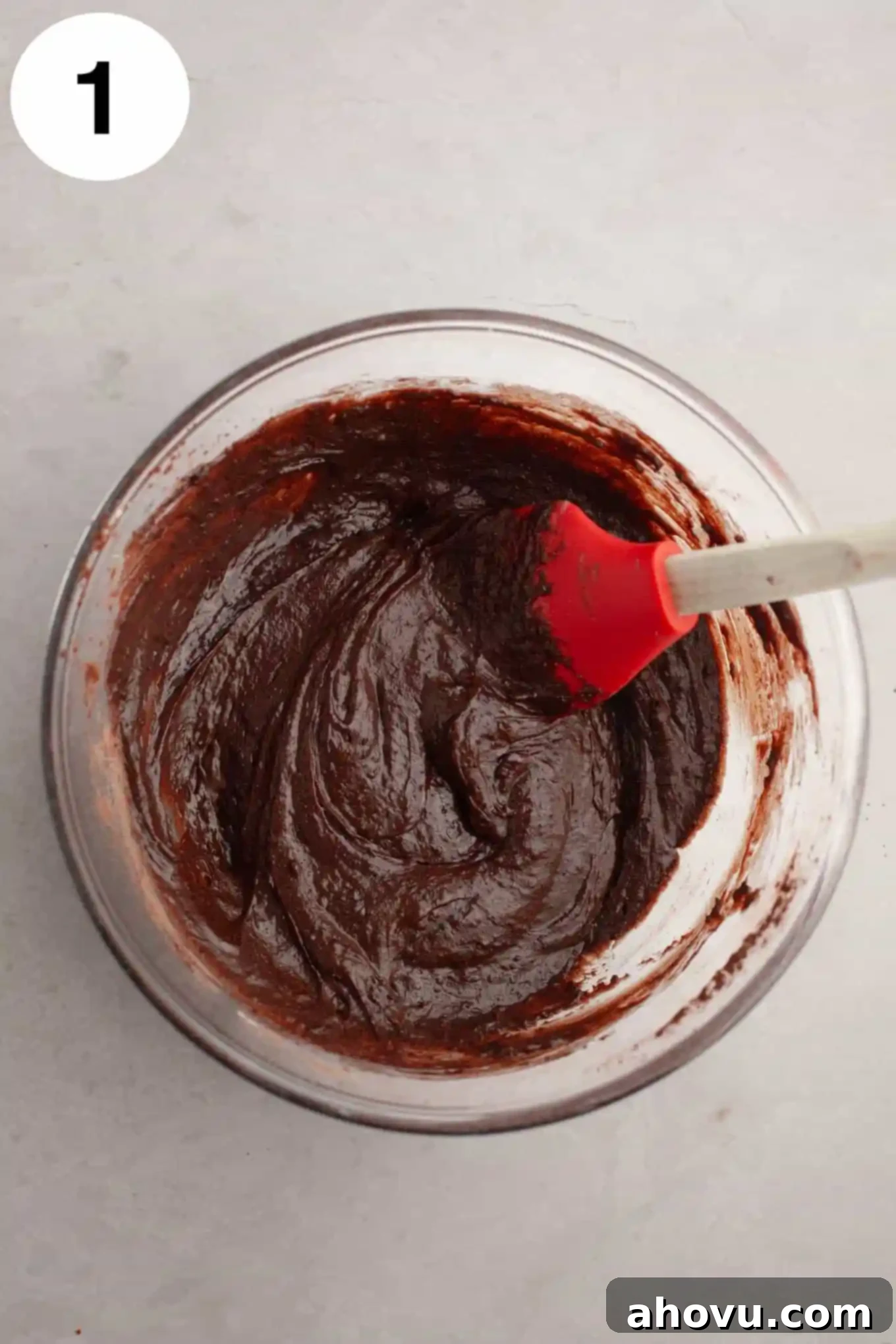 Buckeye Bliss Brownies 4 An overhead view of glossy, raw brownie batter in a clear glass mixing bowl, with a rubber spatula resting inside, ready for baking.