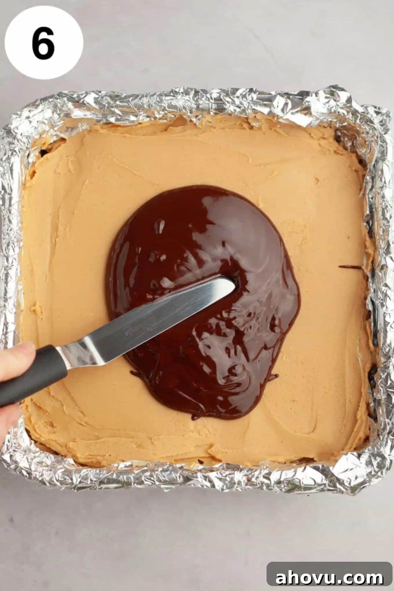 Buckeye Bliss Brownies 9 An overhead process shot showing melted chocolate being carefully spread with an angled spatula over a smooth layer of peanut butter fudge, creating the top layer of Buckeye brownies.