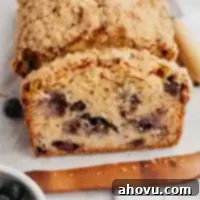 A loaf of blueberry bread that's been sliced on a wooden cutting board.
