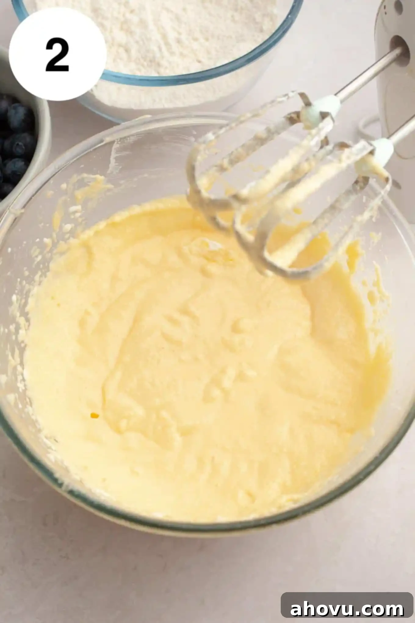 An overhead view of a butter mixture in a glass mixing bowl, with electric beaters. 