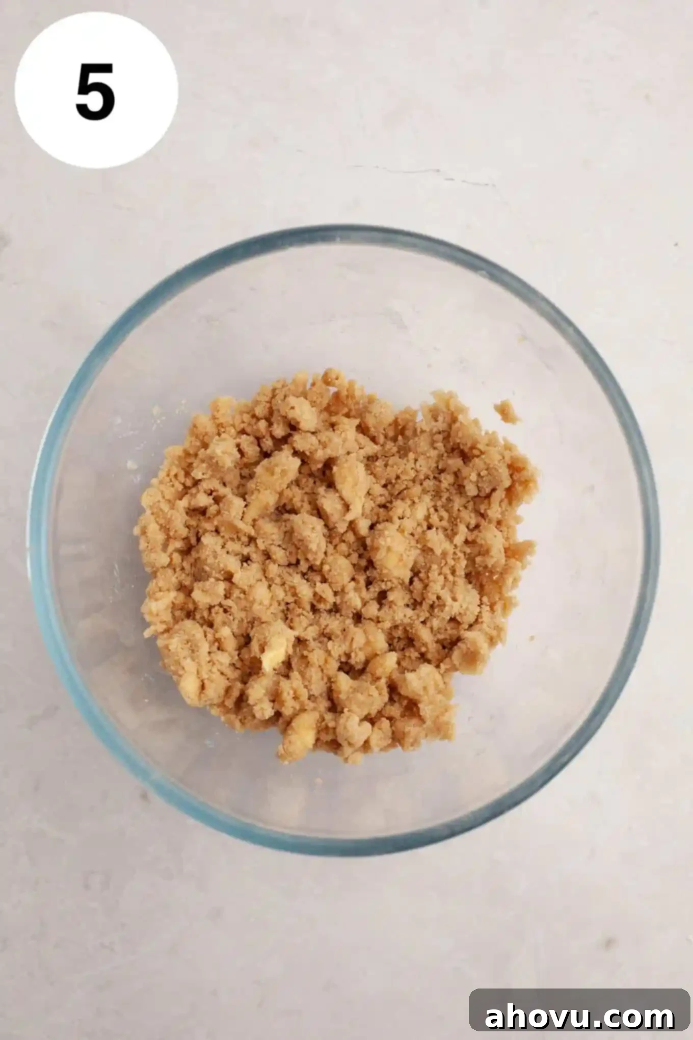 An overhead view of cinnamon streusel in a glass mixing bowl. 