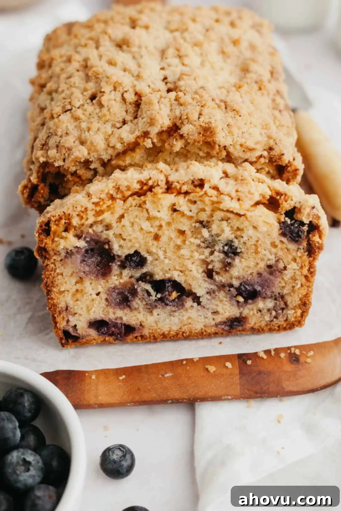 A close-up view of a sliced loaf of blueberry bread topped with streusel. 