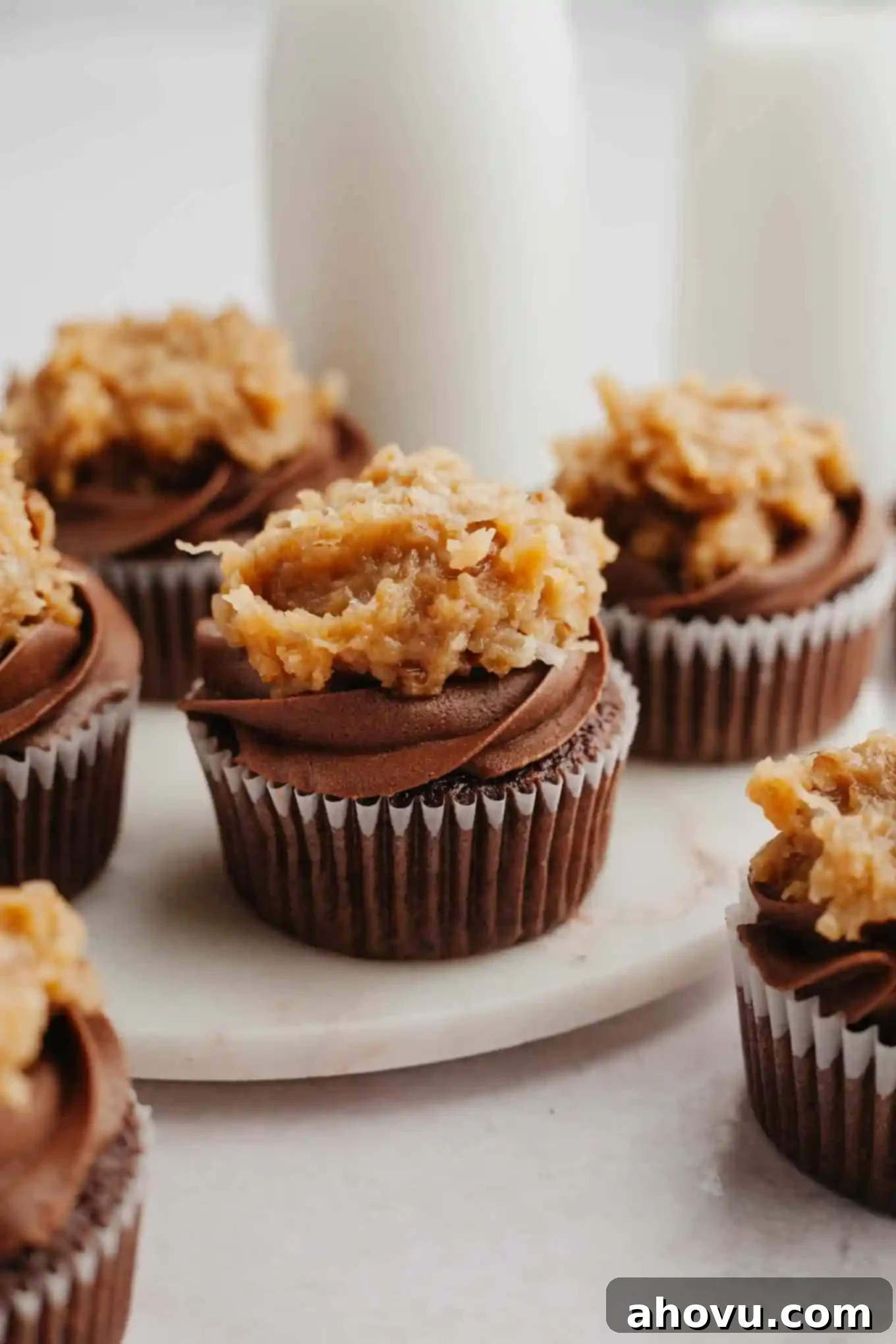 Decadent German Chocolate Cupcakes 2 Frosted German chocolate cupcakes arranged beautifully on a marble serving platter, showcasing their rich chocolate and coconut pecan toppings.
