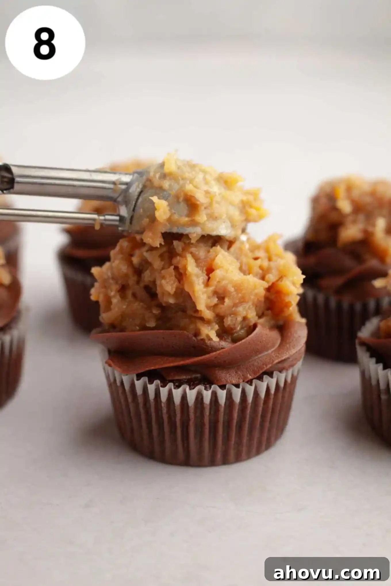 Decadent German Chocolate Cupcakes 12 A process shot demonstrating German chocolate frosting being carefully dolloped onto the center of a chocolate cupcake, filling the space within the piped chocolate border.