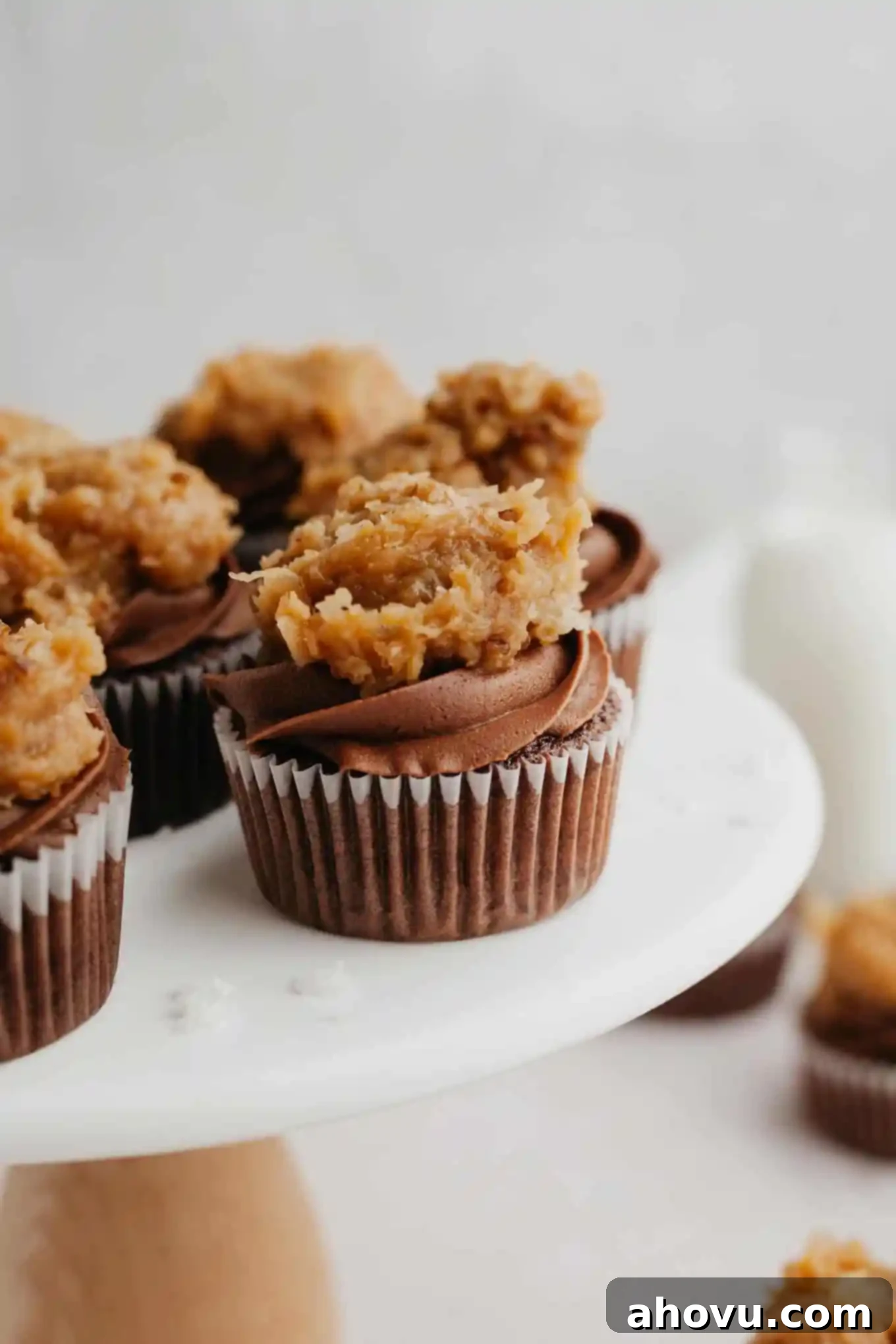 Decadent German Chocolate Cupcakes 13 A beautiful side view of several perfectly frosted German chocolate cupcakes, showcasing their dual frosting layers, elegantly arranged on a marble cake stand.