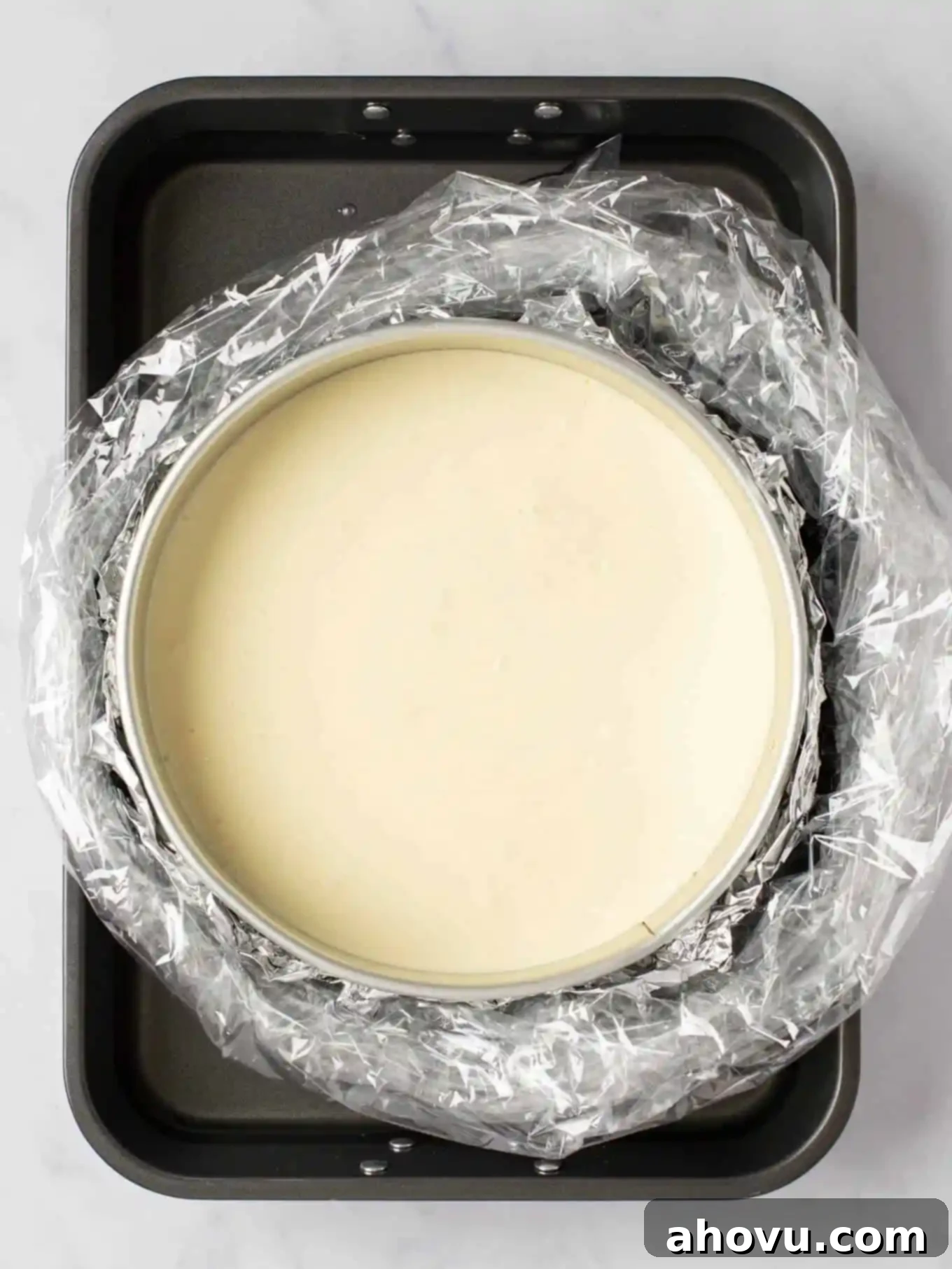 Your Guide to a Perfect Cheesecake Water Bath 2 A cheesecake in a springform pan that's wrapped in foil and an oven bag. The wrapped pan is sitting inside of a large roasting pan with hot water.