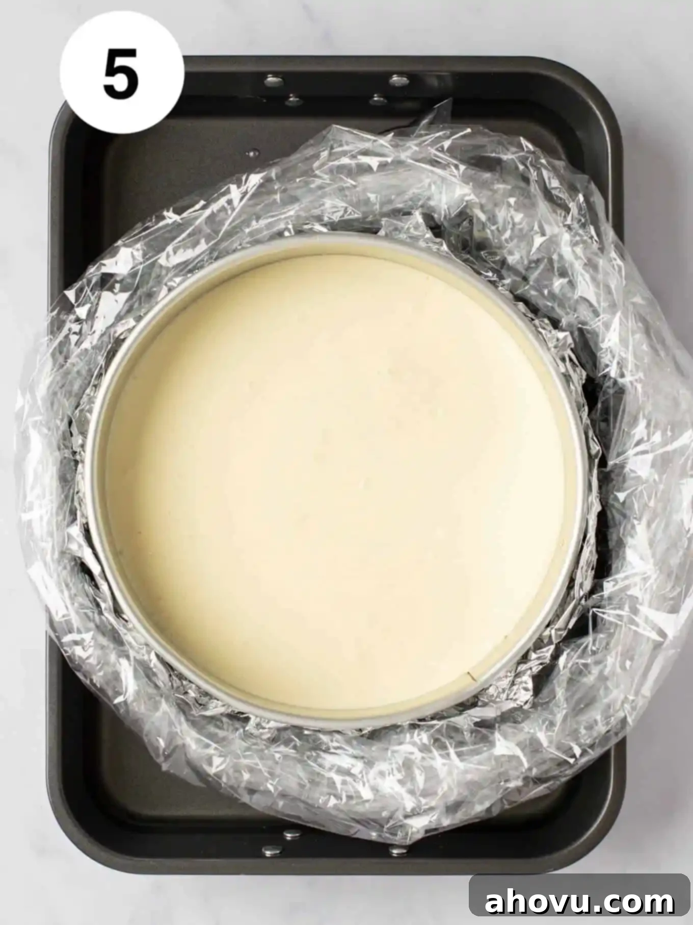 Your Guide to a Perfect Cheesecake Water Bath 9 A cheesecake in a springform pan that's wrapped in foil and an oven bag and is sitting inside of a water bath.