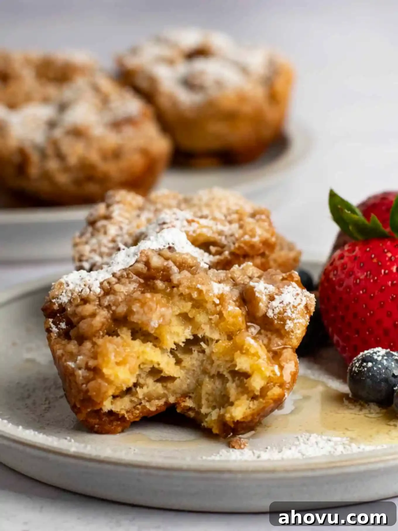 Two French toast muffins on a plate with fresh fruit. The muffin in the front has a bite missing.