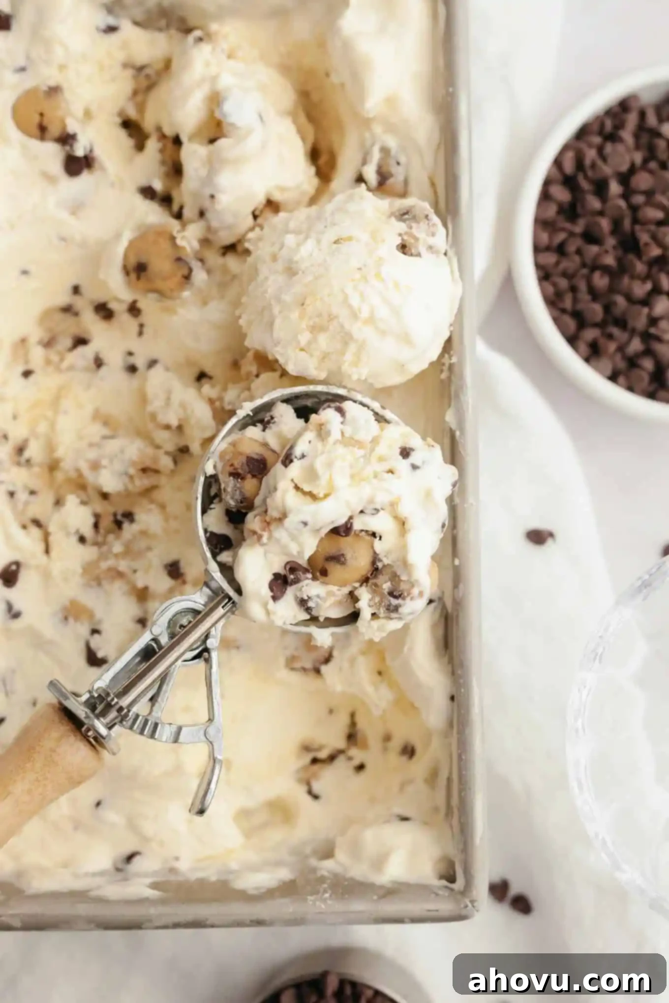 An overhead view of an ice cream scoop full of cookie dough ice cream, resting on a pan of ice cream. 