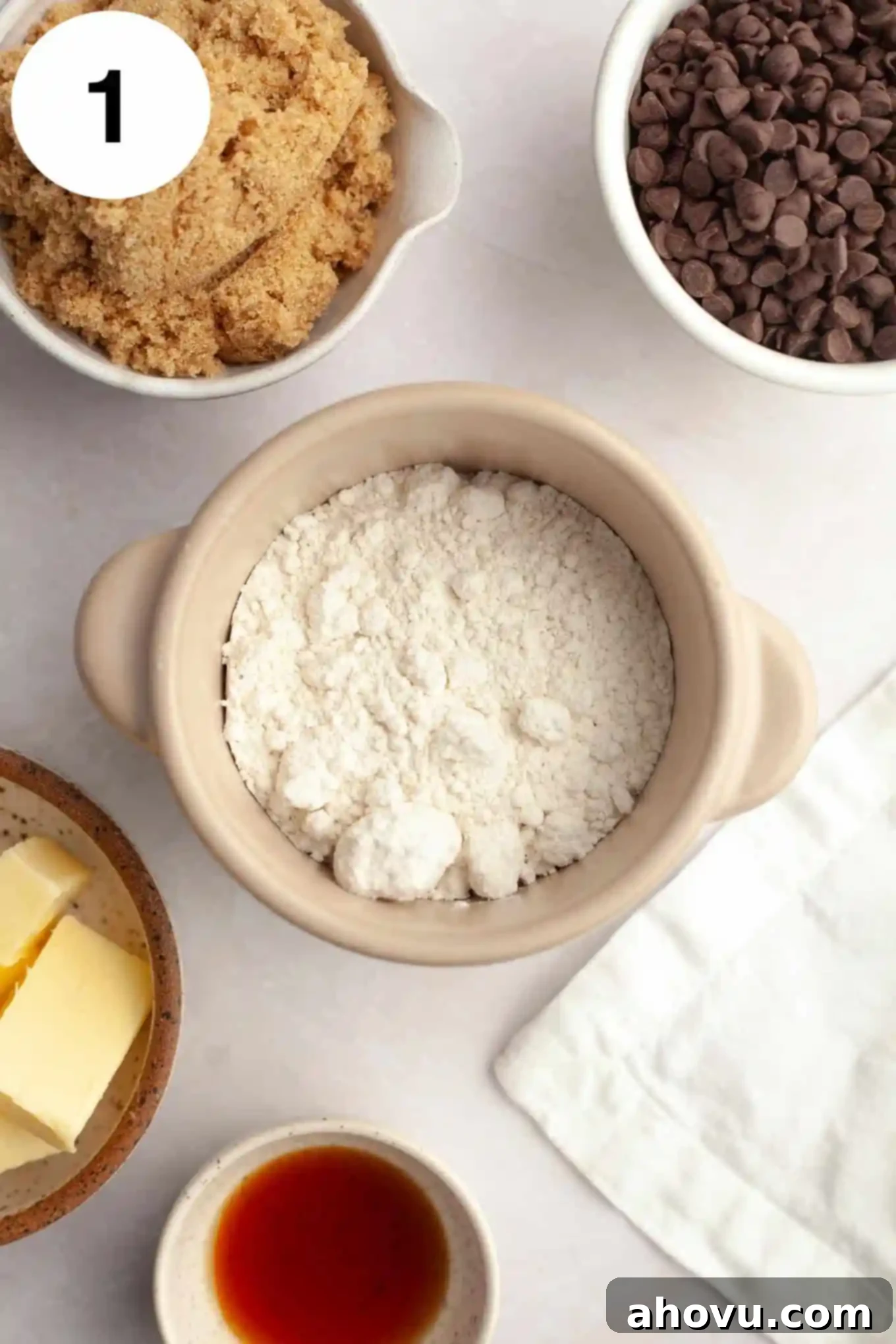 An overhead view of individual bowls of brown sugar, chocolate chips, flour, butter, and vanilla. 