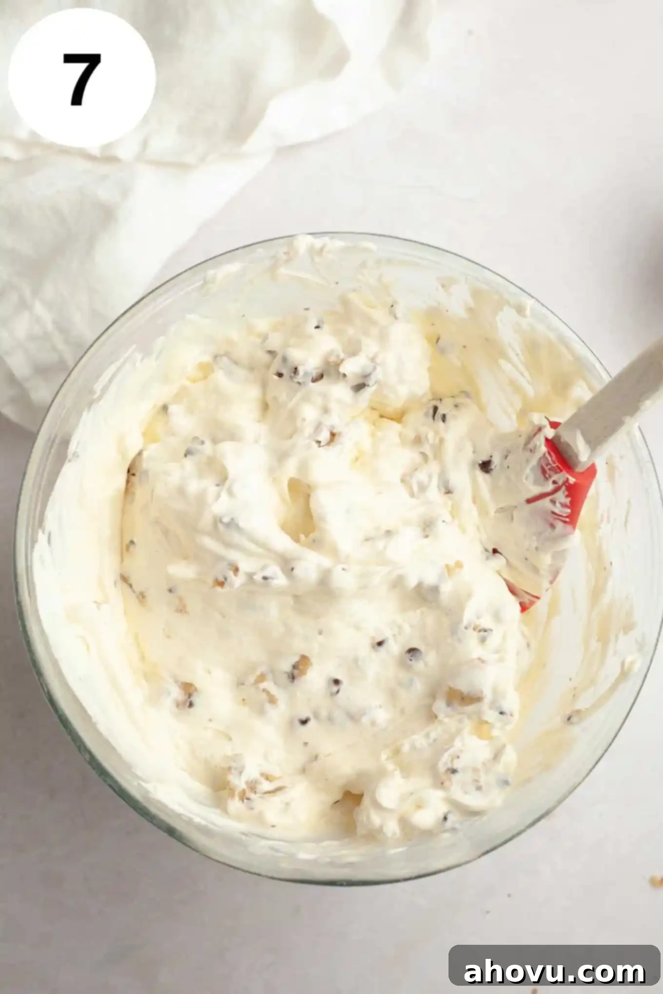 An overhead view of chocolate chip cookie dough ice cream in a glass mixing bowl, with a rubber spatula. 