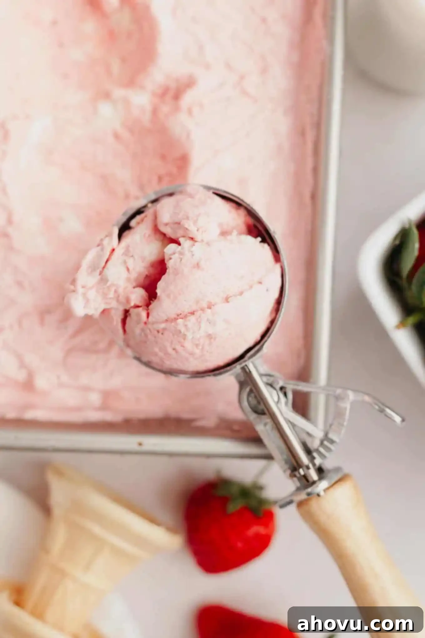 A scoop of rich, creamy strawberry ice cream held elegantly over a pan of the frozen treat, highlighting its perfect texture.
