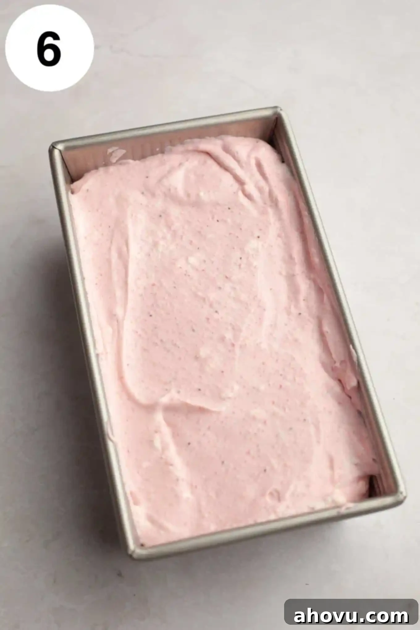 An overhead view of the smooth strawberry ice cream mixture expertly transferred into a metal loaf pan, ready for the freezing process.