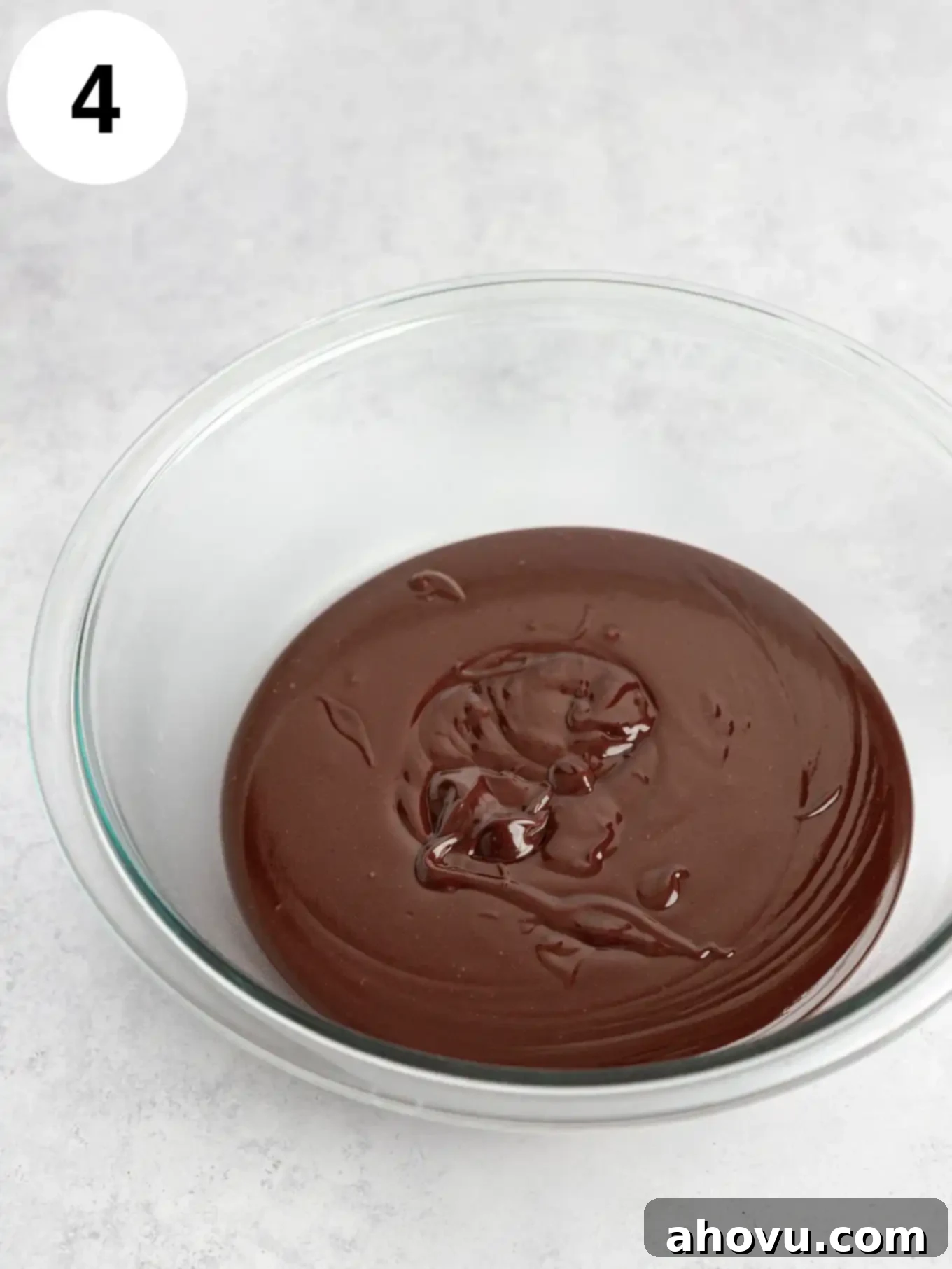 A close-up view of a clear glass bowl filled with warm, glossy, and perfectly smooth hot fudge sauce, ready to be enjoyed.