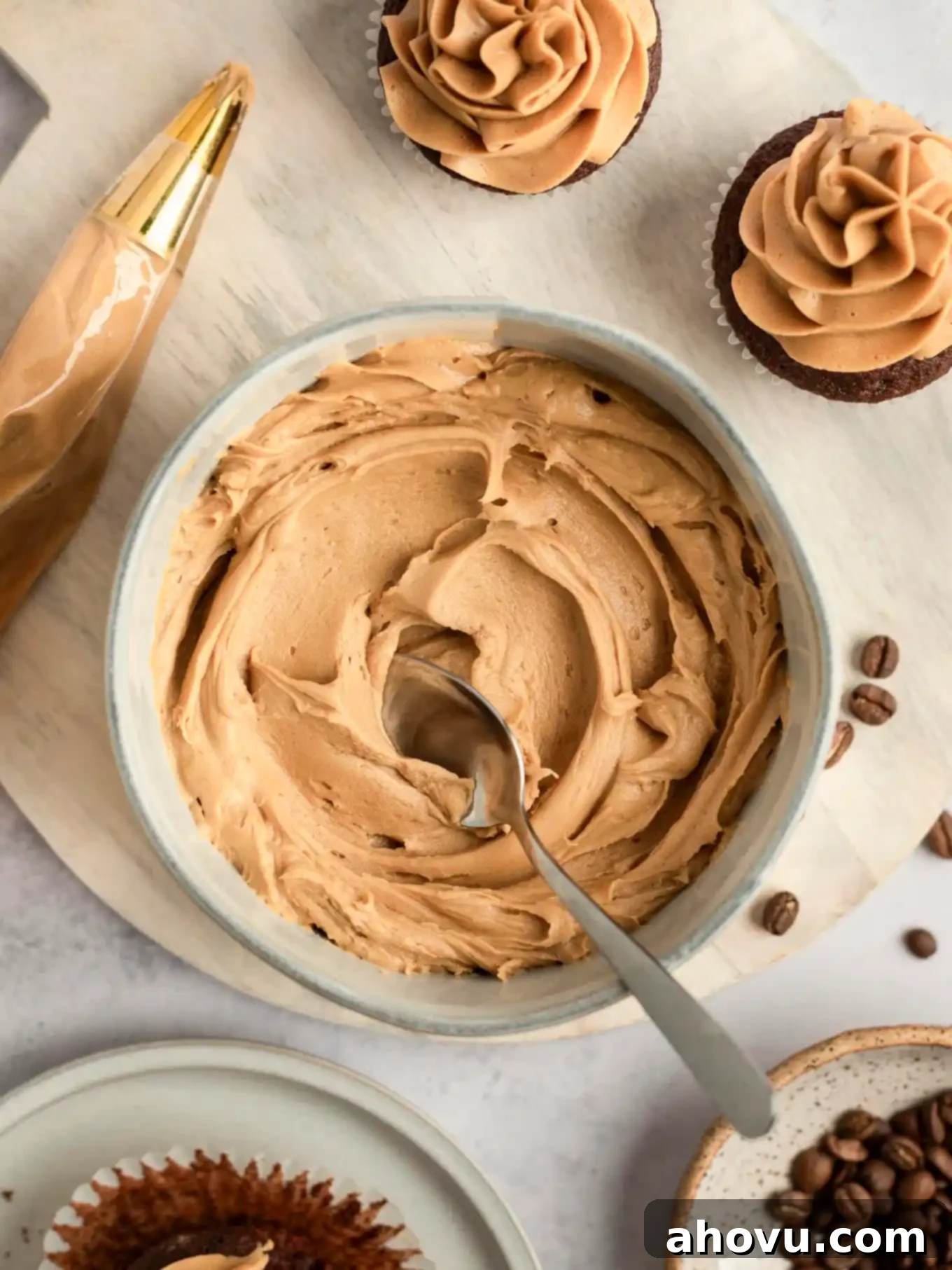 An overhead view of a bowl of coffee buttercream frosting, with two cupcakes. 