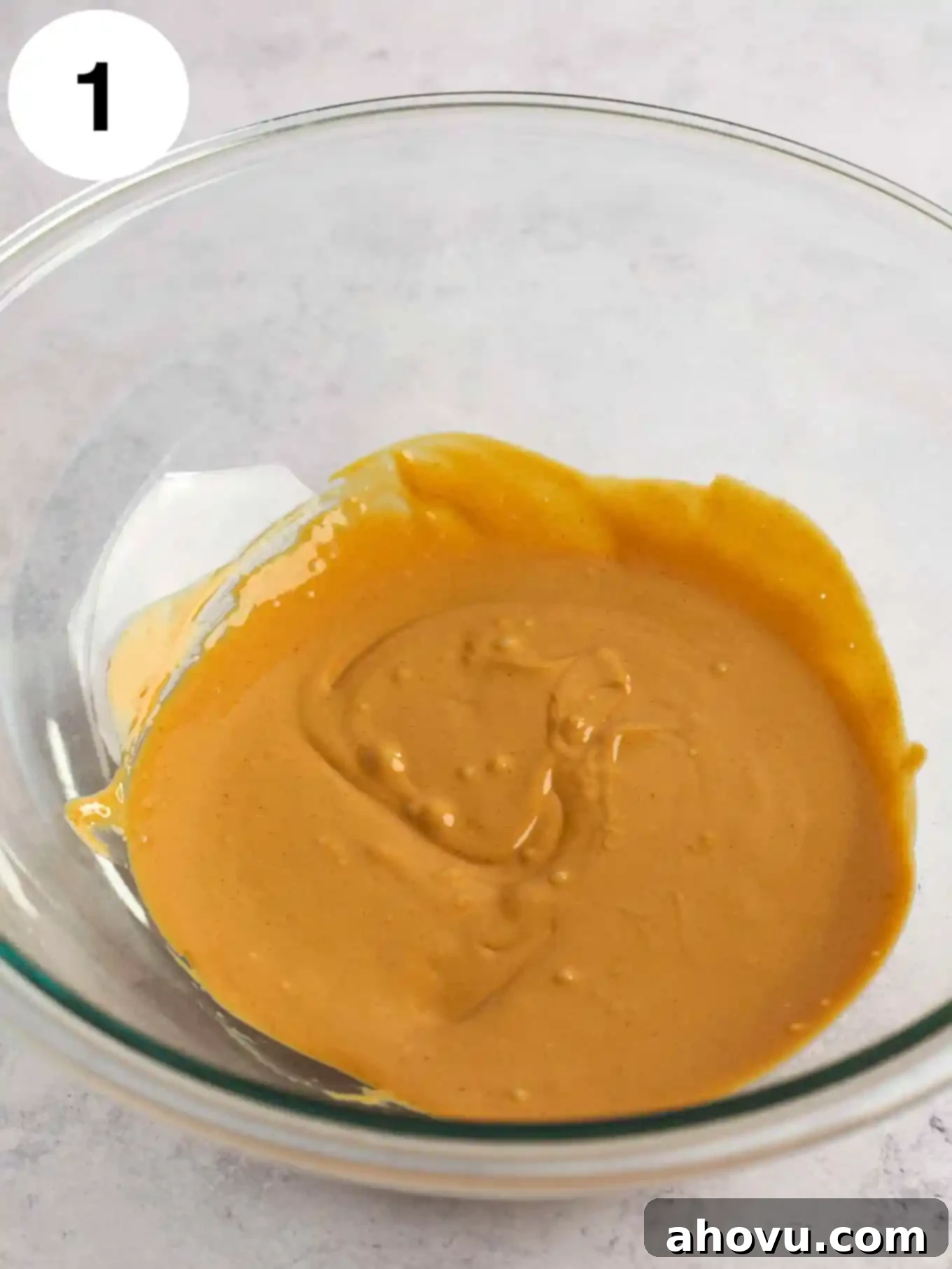 Velvet Peanut Butter Freeze 4 Melted creamy peanut butter in a clear glass mixing bowl, ready for the next step.