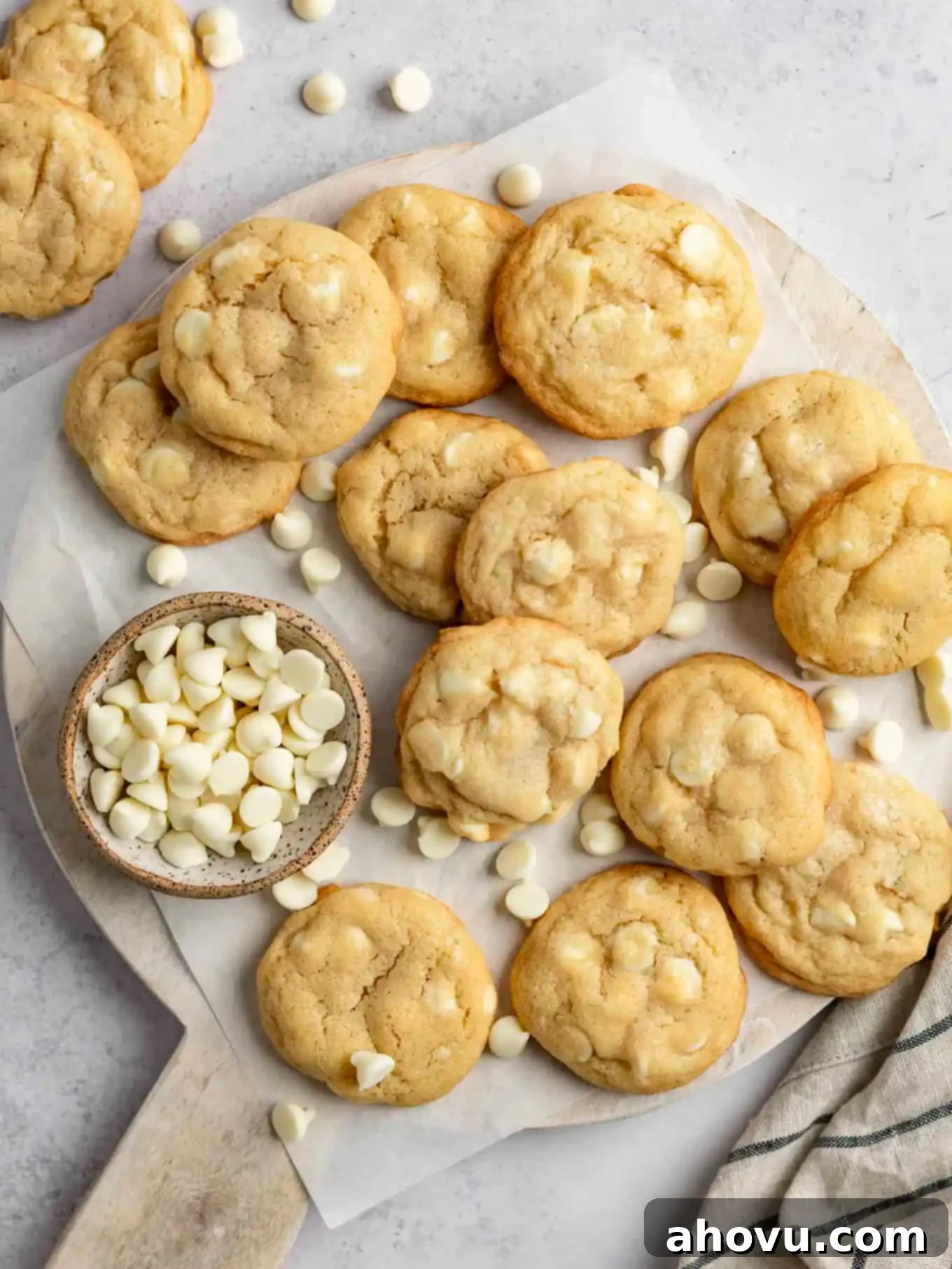 An overhead view of warm, golden white chocolate chip cookies cooling on a wooden cutting board, showcasing their soft texture and abundant white chocolate chunks.