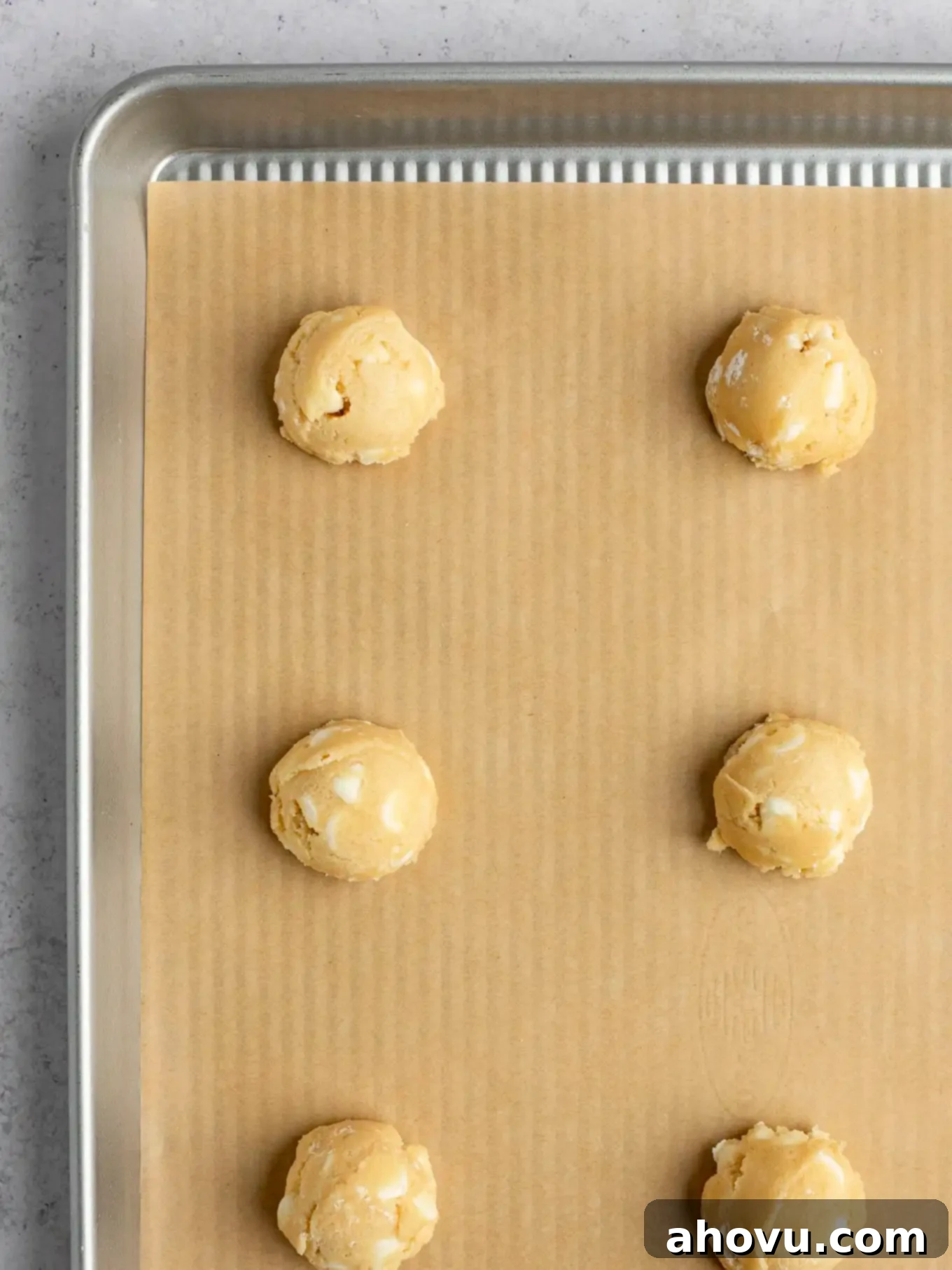 Perfectly portioned scoops of white chocolate chip cookie dough arranged on a baking sheet lined with brown parchment paper, ready for chilling and baking.