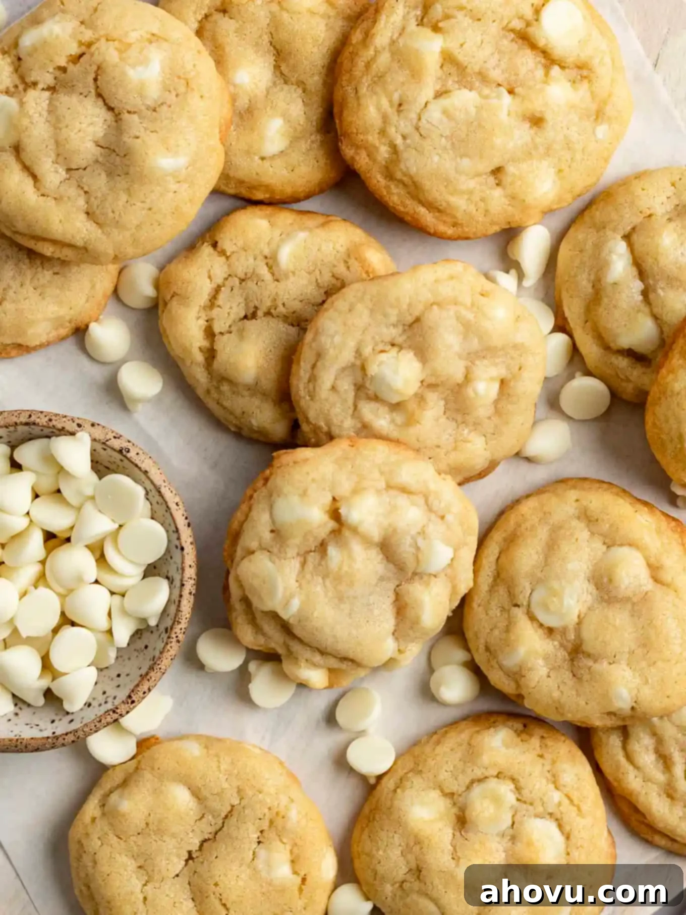 An overhead view of freshly baked white chocolate chip cookies cooling on parchment paper, highlighting their golden-brown edges and soft centers.