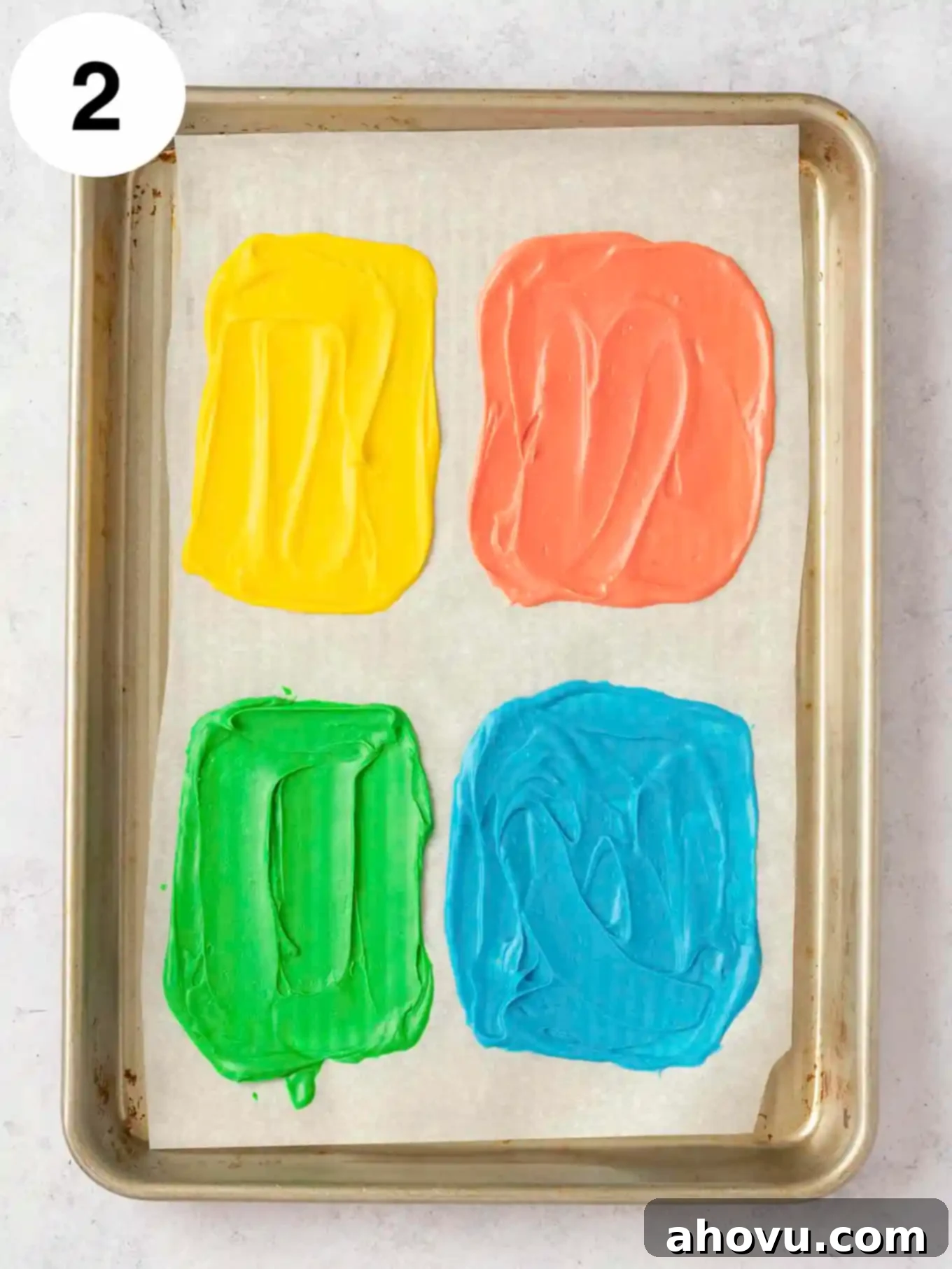 Joyful Confetti Frosting 5 An overhead view of four rectangles of colored melted white chocolate on a baking sheet.