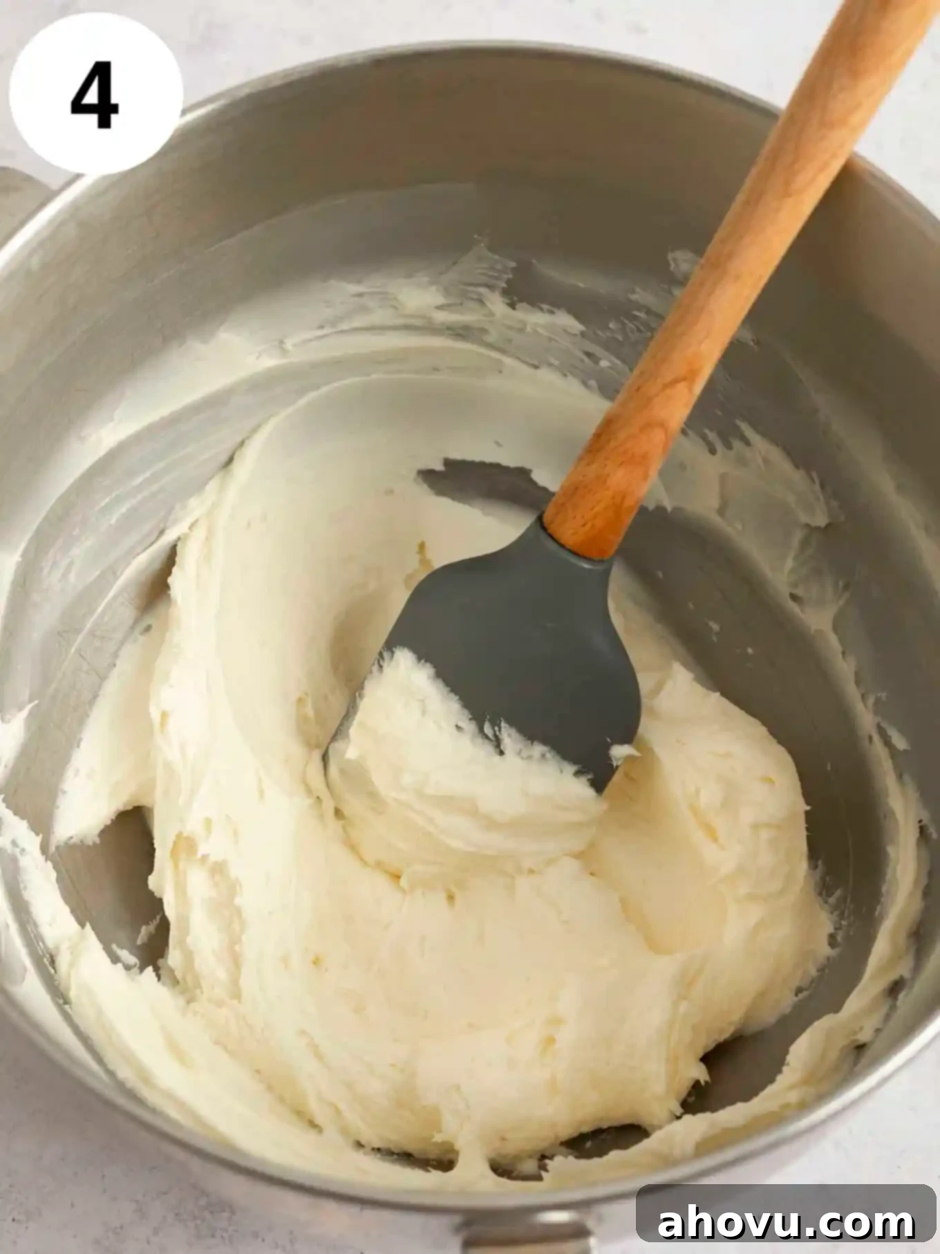 Joyful Confetti Frosting 7 An overhead view of white frosting in a mixing bowl, with a rubber spatula.