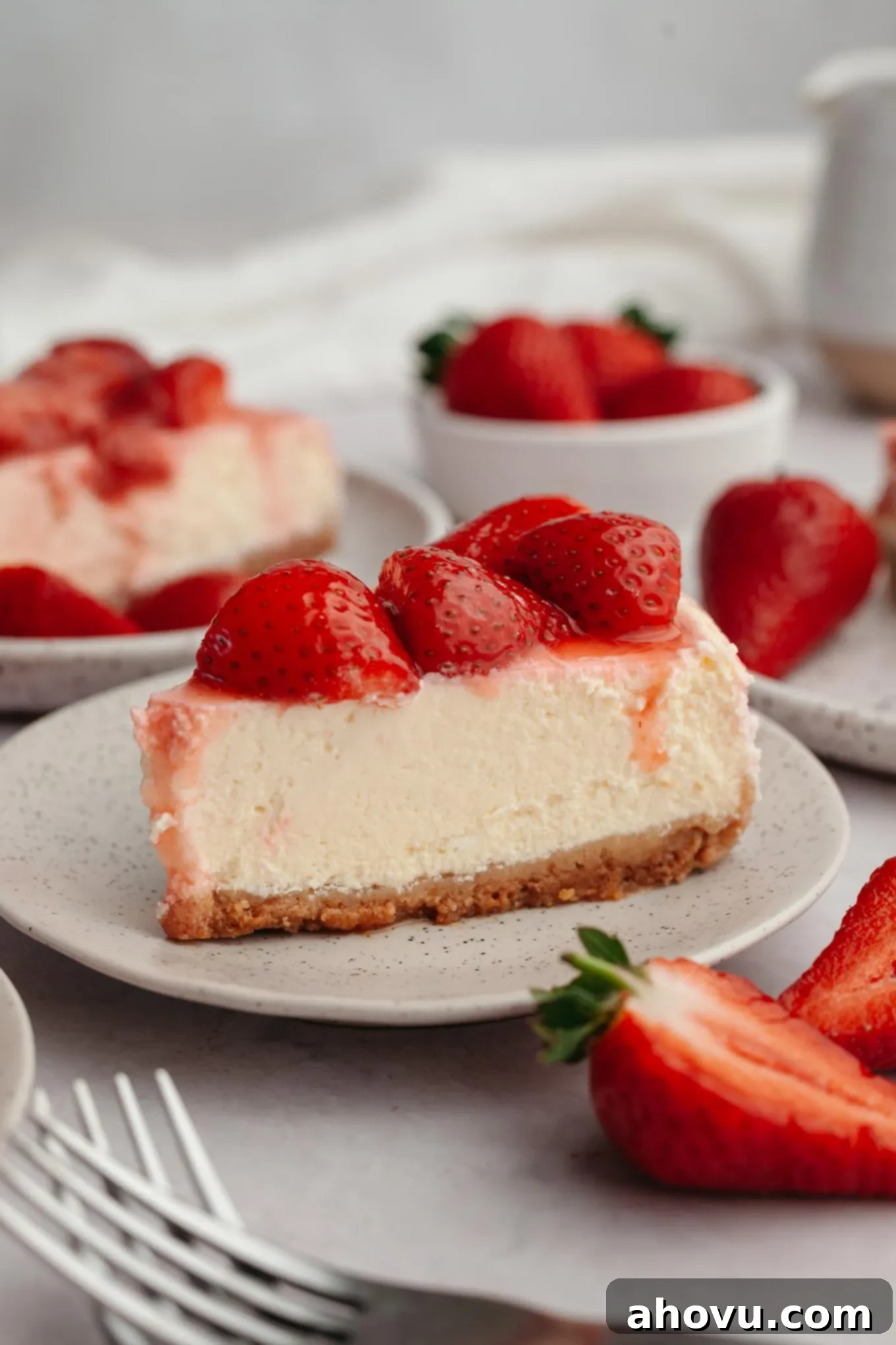 A beautiful slice of strawberry cheesecake on a white plate, showcasing the layers of crust, creamy filling, and glistening berry topping.