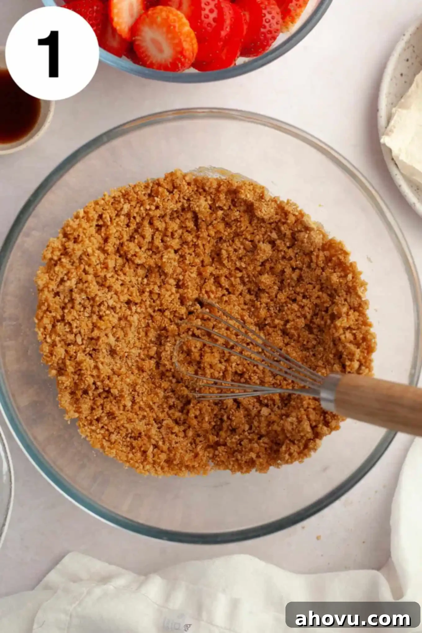 An overhead shot showing golden graham cracker crumbs perfectly mixed in a glass bowl, ready for the crust preparation.