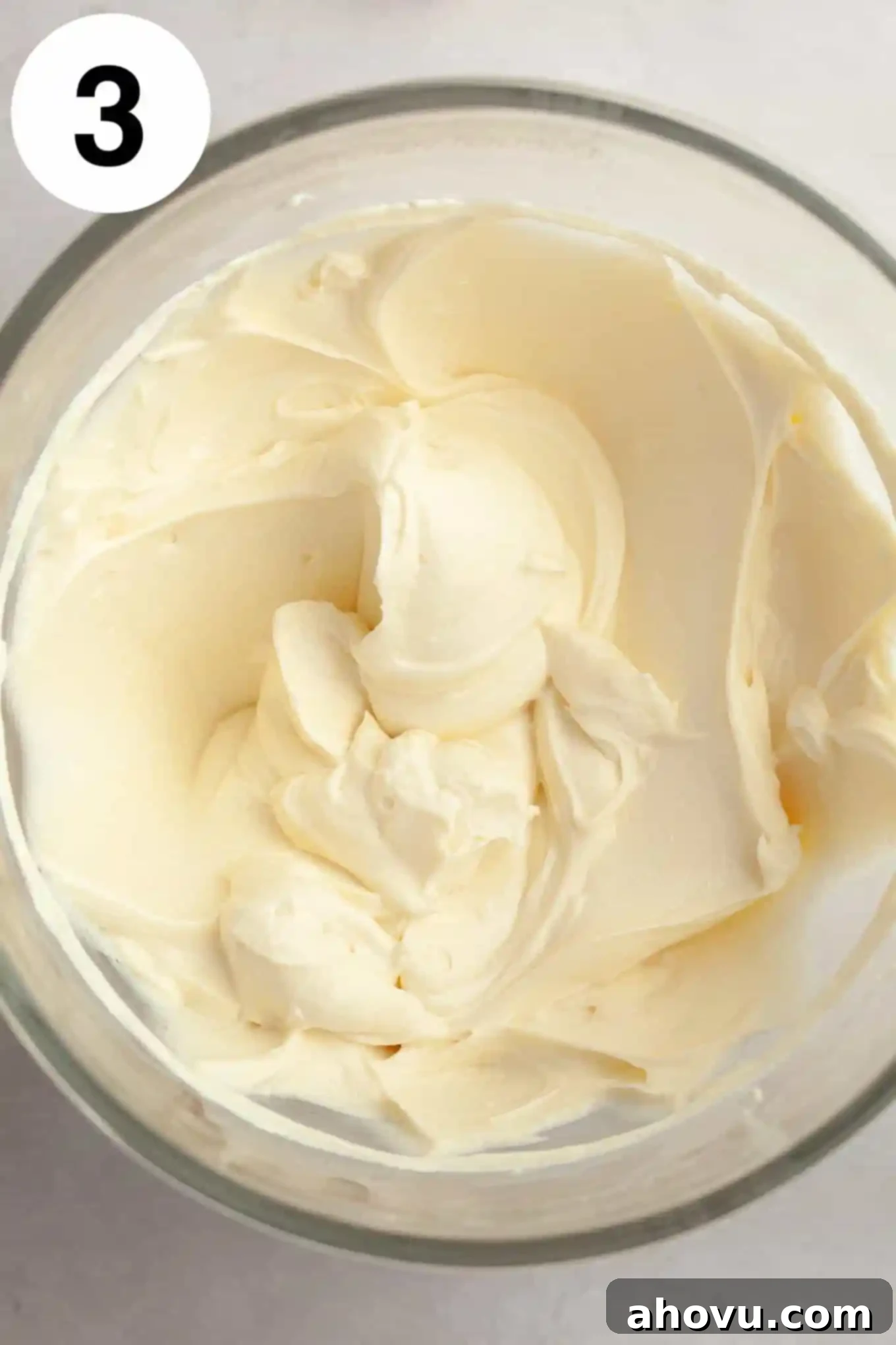 An overhead view of smooth, creamy beaten cream cheese and sour cream in a glass mixing bowl, perfectly blended.