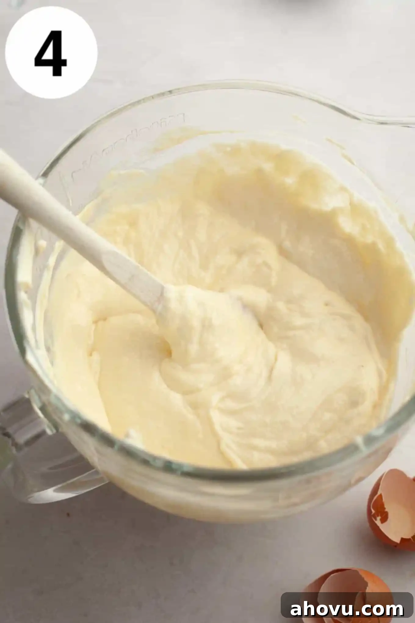 An overhead shot of rich, velvety cheesecake filling in a glass mixing bowl, ready to be poured into the crust.