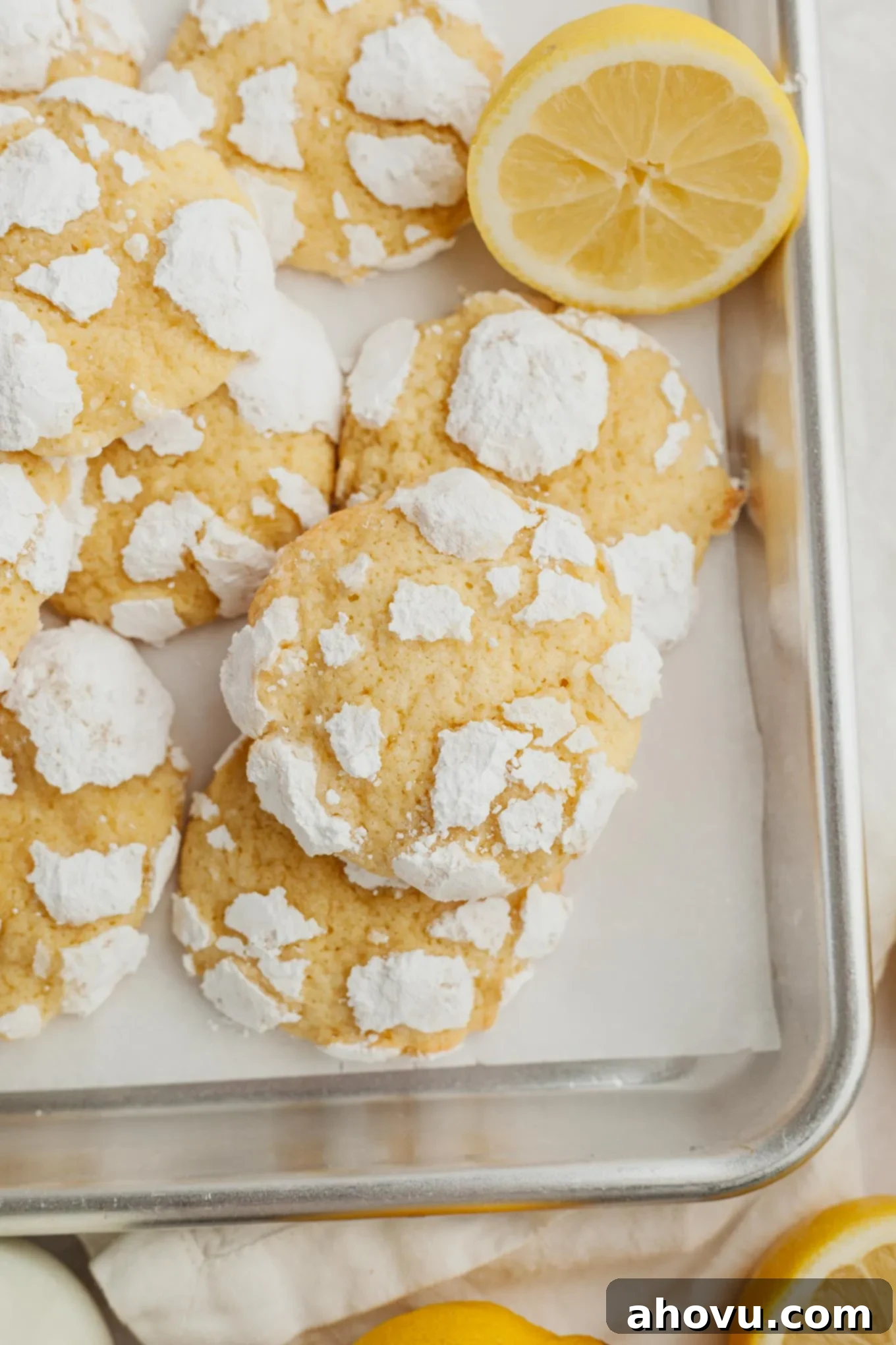 An overhead view of freshly baked, perfectly crinkled lemon cookies cooling on a parchment paper-lined baking tray.