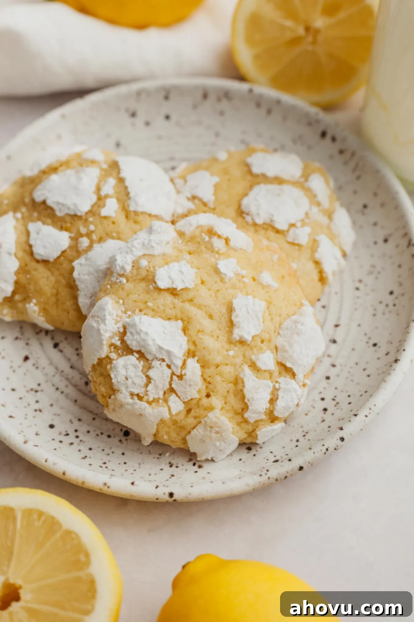 Three perfectly baked lemon crinkle cookies arranged neatly on a speckled white dessert plate, highlighting their texture and sugar coating.