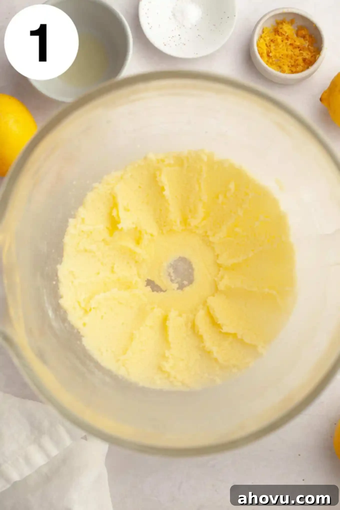 An overhead view of softened unsalted butter and granulated sugar being creamed together in a glass mixing bowl with an electric mixer.