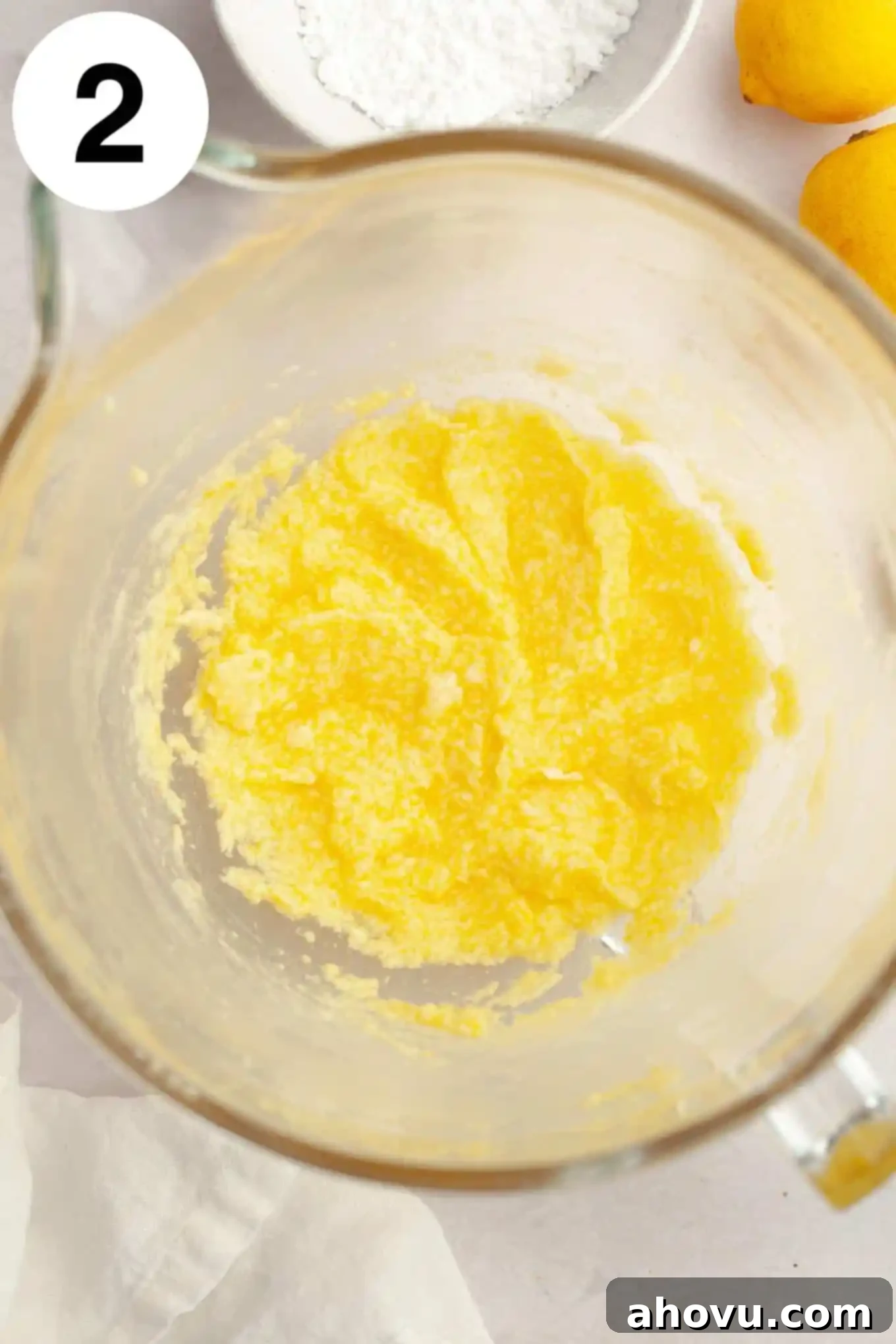 An overhead view of the wet ingredients—creamed butter, sugar, egg, lemon juice, zest, and extract—blended smoothly in a glass mixing bowl.
