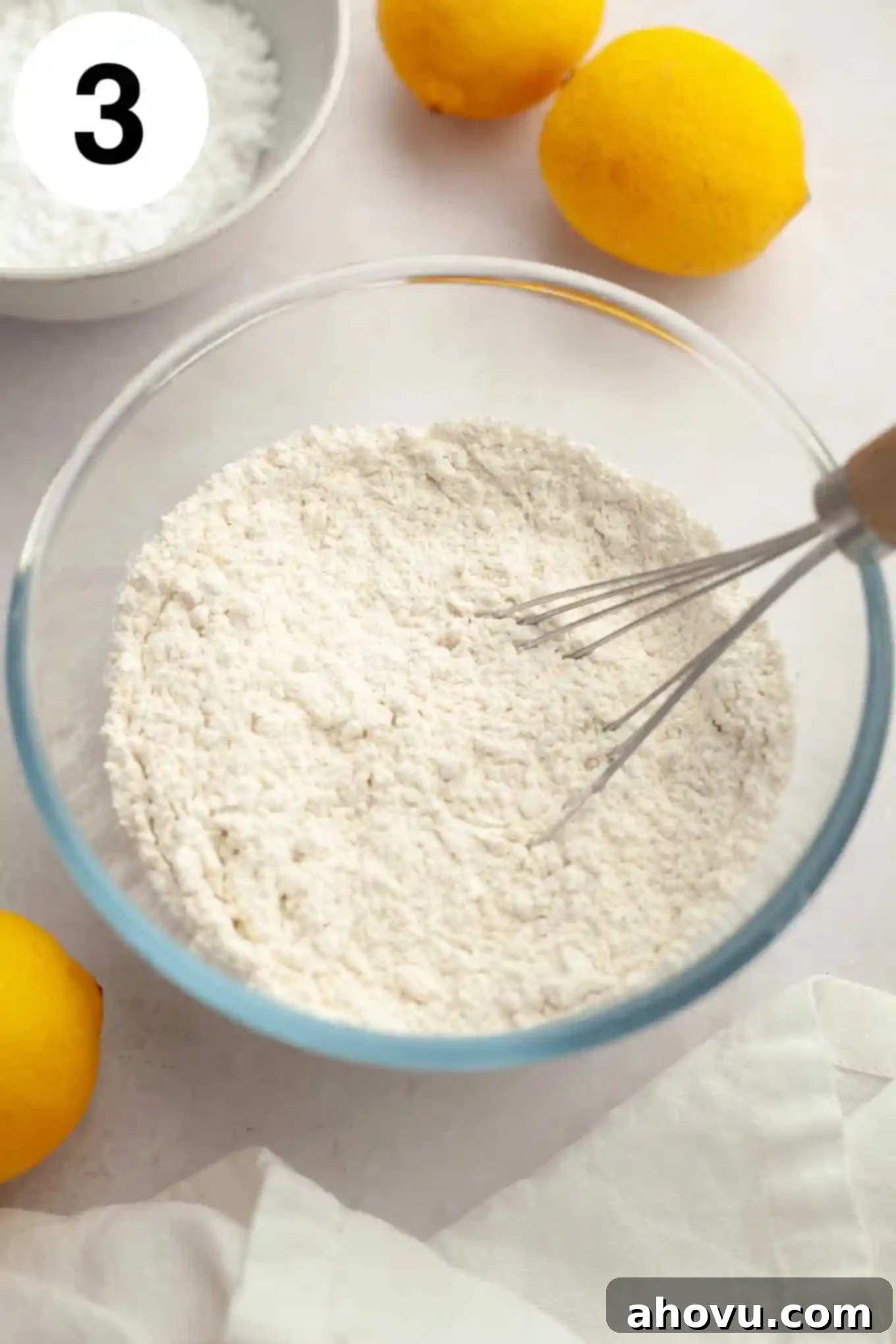 An overhead view of all-purpose flour, salt, and baking powder being whisked together in a separate glass mixing bowl.