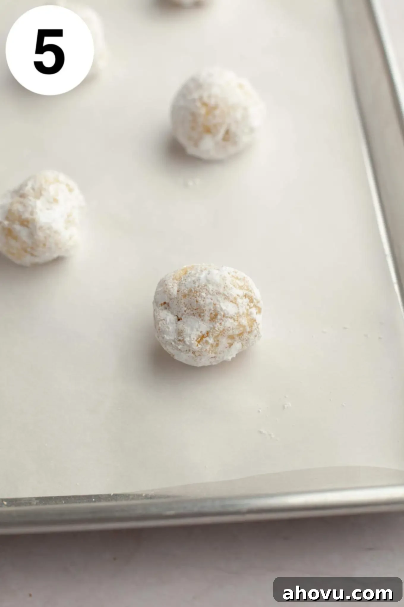 Raw lemon crinkle cookie dough balls, generously coated in granulated and powdered sugar, arranged on a parchment paper-lined baking sheet before baking.