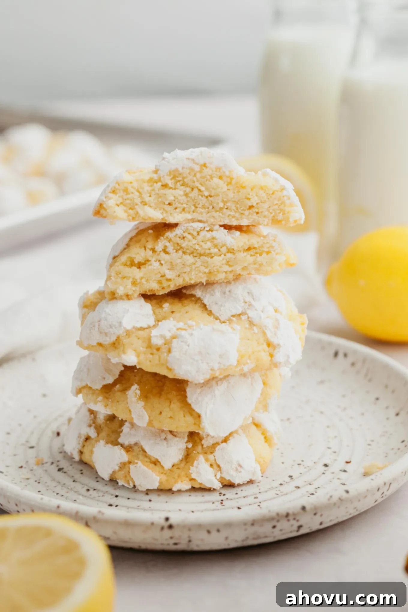 A delightful stack of three perfectly baked lemon crinkle cookies, showcasing their white powdered sugar coating and soft texture, presented on a speckled dessert plate.