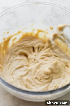 A glass mixing bowl holds the thoroughly combined wet ingredients for the cookie dough, showcasing their creamy, uniform texture before dry ingredients are added.