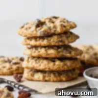 A stack of golden oatmeal raisin cookies on a small cooling rack, set against a backdrop of parchment paper.