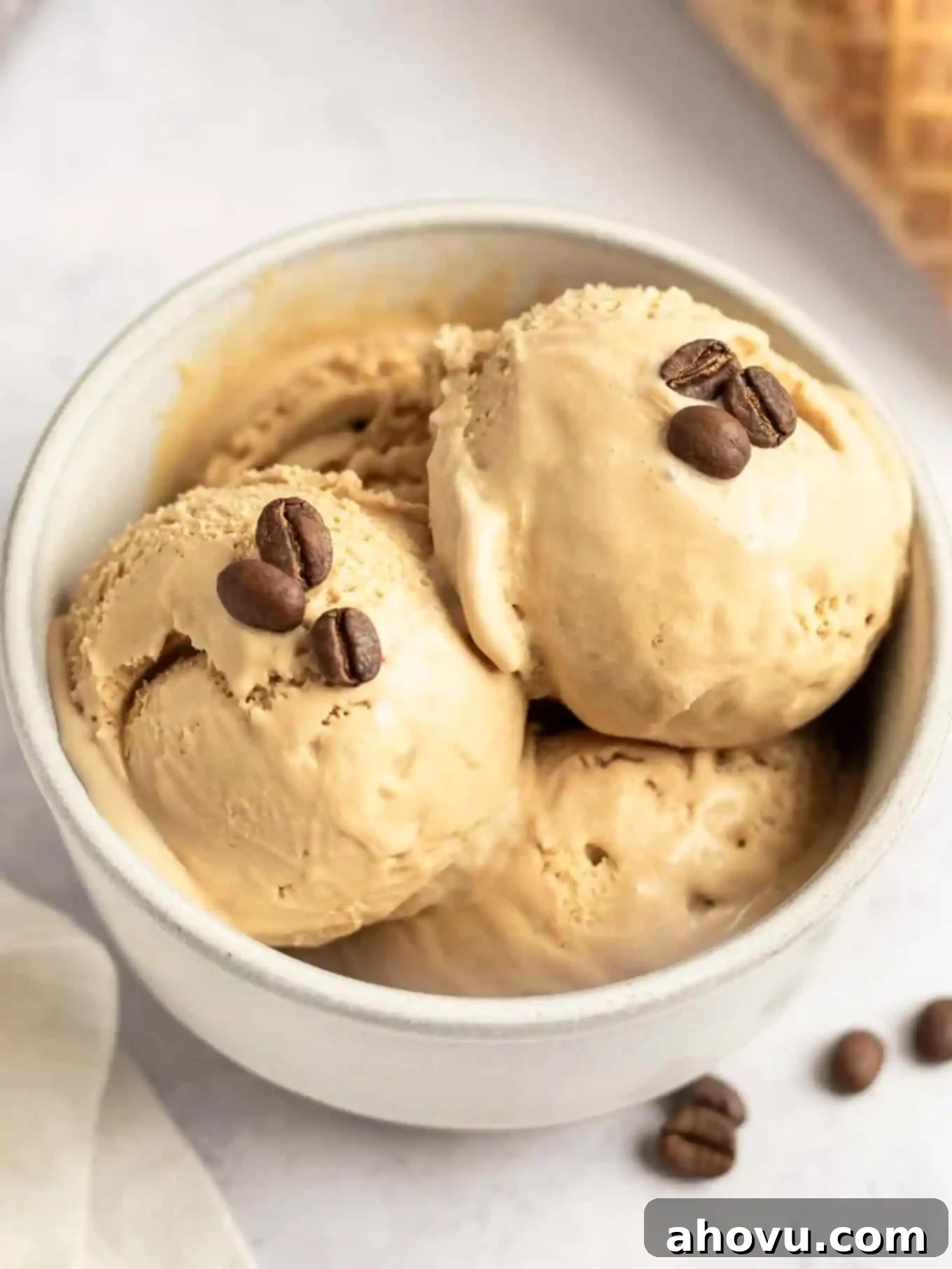 Three scoops of homemade no-churn coffee ice cream in a white ceramic bowl, garnished with a coffee bean.