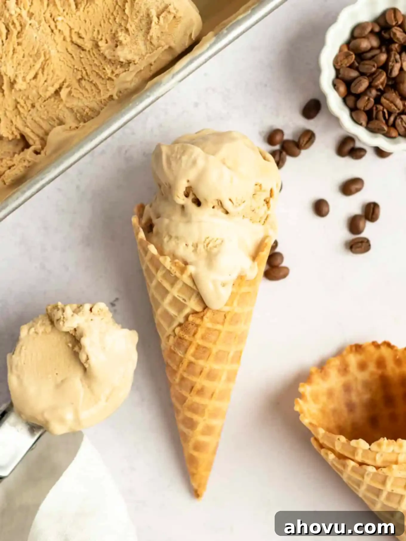 An overhead shot of a coffee ice cream cone lying on its side, surrounded by scattered coffee beans and additional empty waffle cones, evoking a rustic and inviting feel.