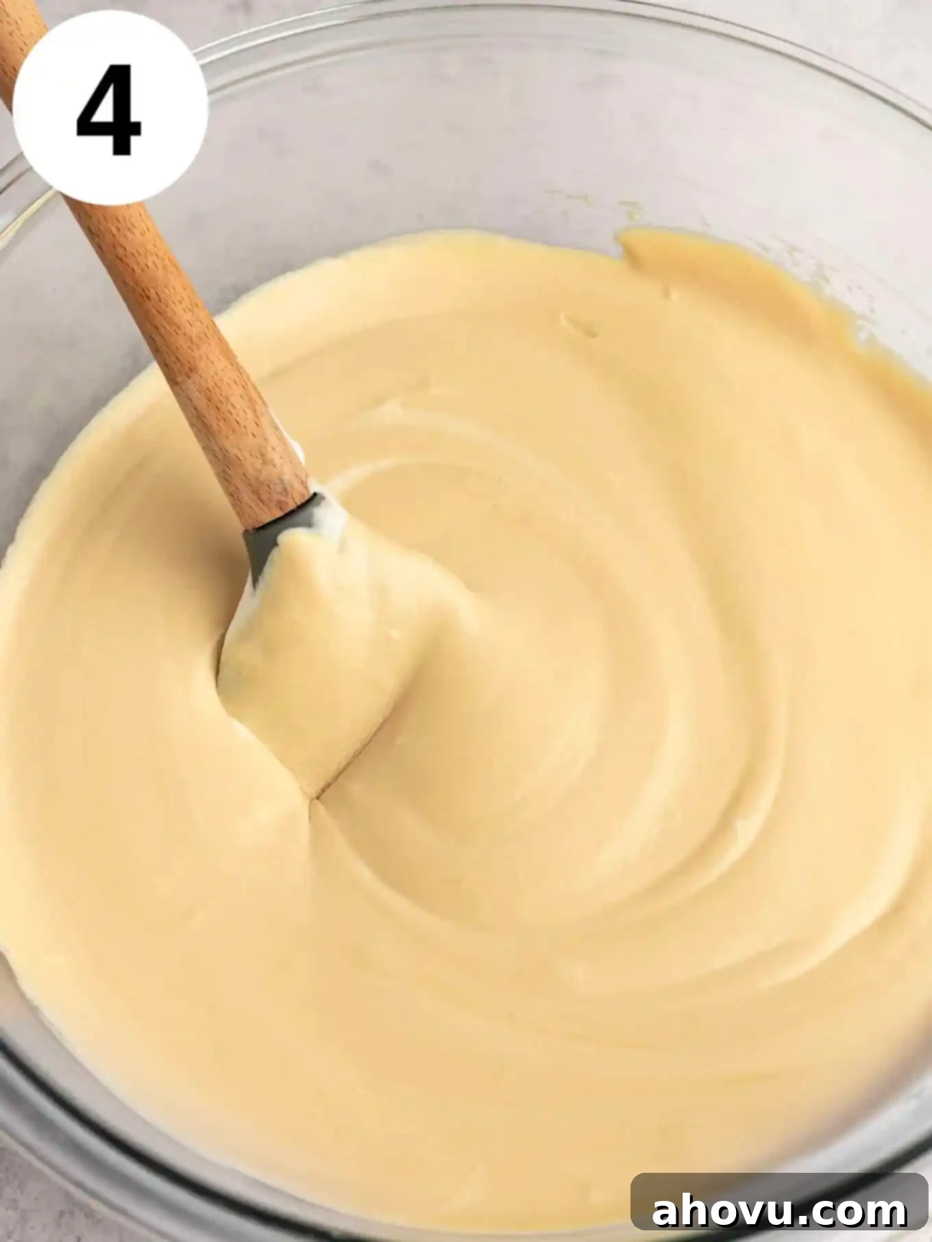 A glass mixing bowl with the combined coffee ice cream base and gently folded whipped cream, with a rubber spatula resting in the mixture.
