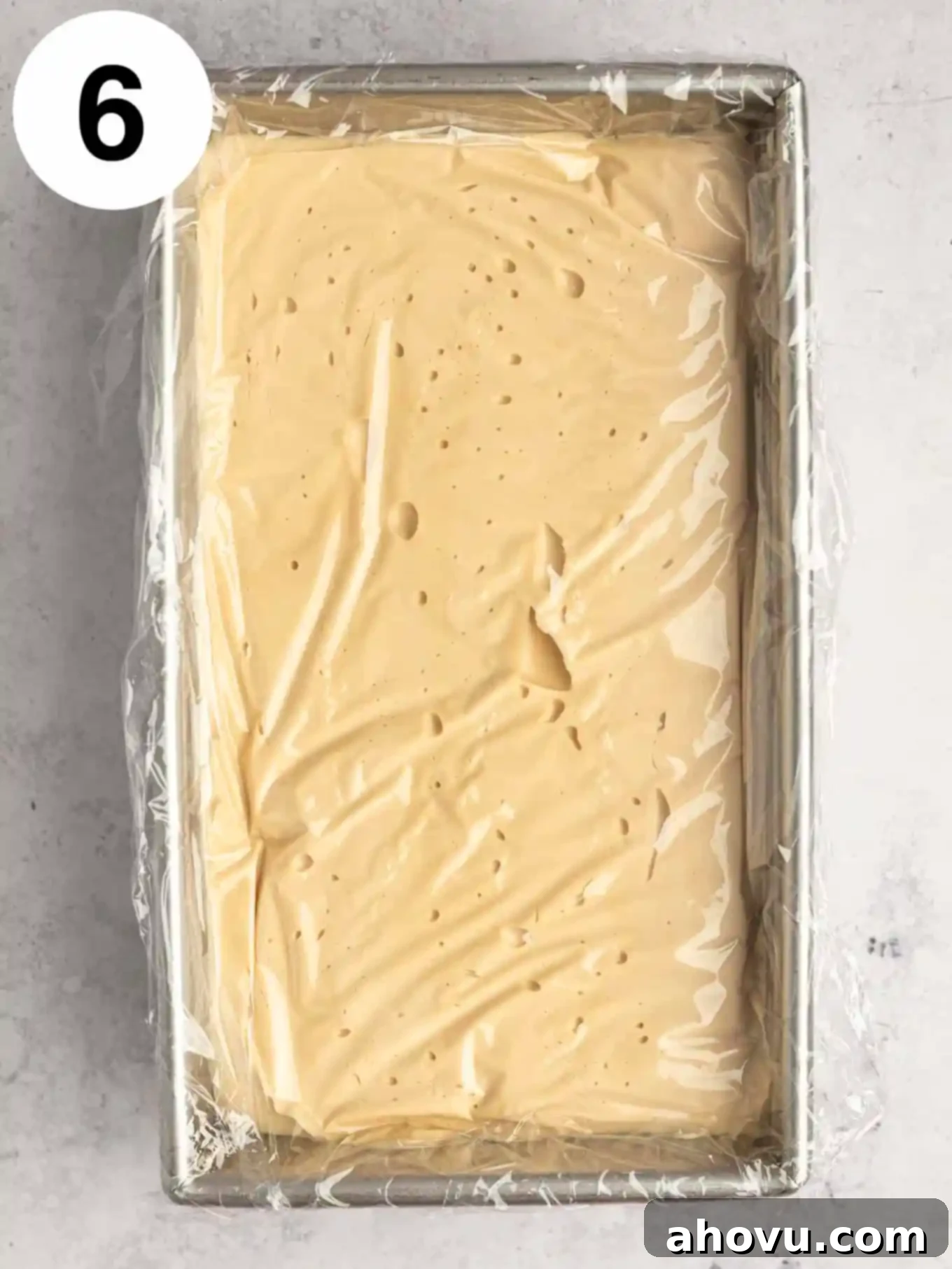 A loaf pan filled with coffee flavored ice cream, securely covered with plastic wrap pressed directly onto the surface.