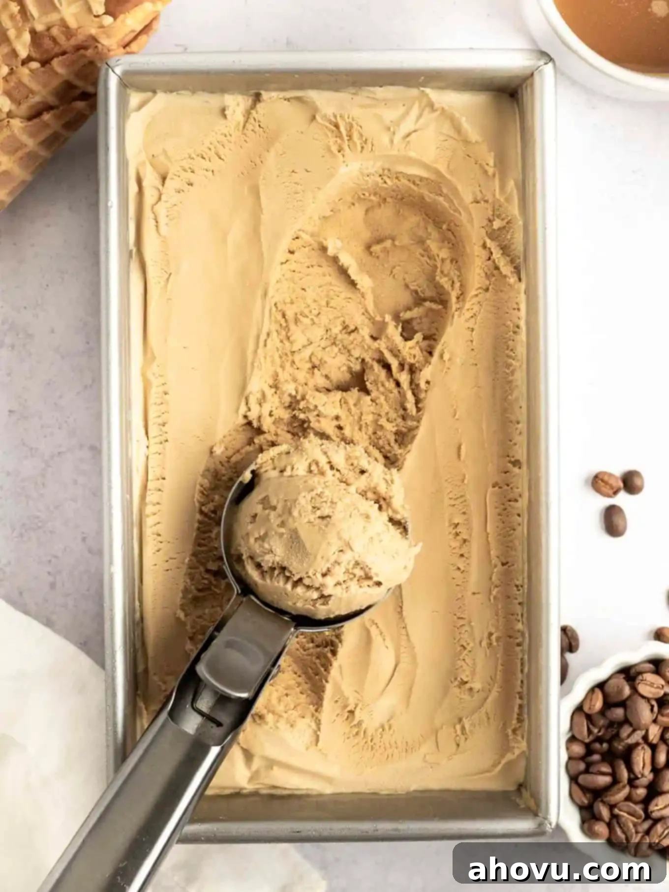 A loaf pan of perfectly frozen coffee ice cream with an ice cream scoop resting on top, ready for serving.