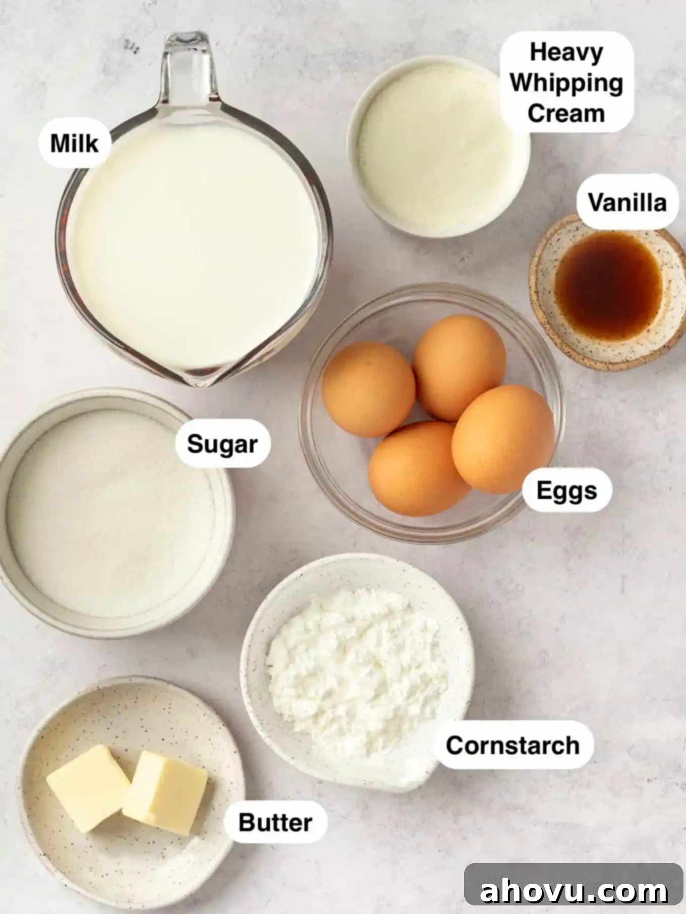 Creamy Vanilla Dream 3 An overhead view of the essential ingredients for homemade vanilla pudding, neatly arranged and ready for preparation, including granulated sugar, cornstarch, egg yolks, heavy whipping cream, whole milk, unsalted butter, and pure vanilla extract.