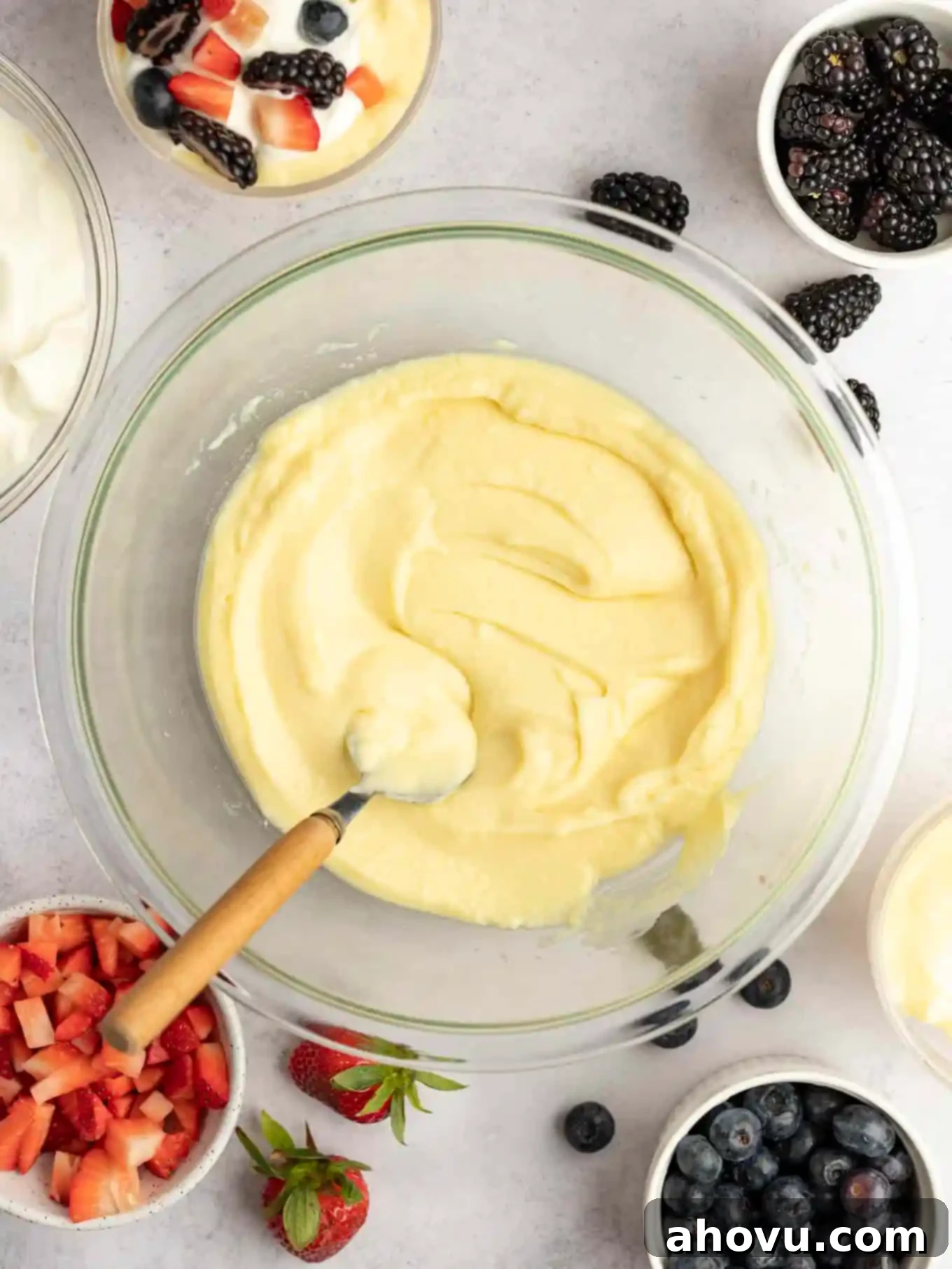 Creamy Vanilla Dream 10 An overhead view of homemade vanilla pudding in a large glass bowl, surrounded by smaller dishes of fresh berries like strawberries, blueberries, and raspberries, illustrating delicious serving suggestions for this classic dessert.