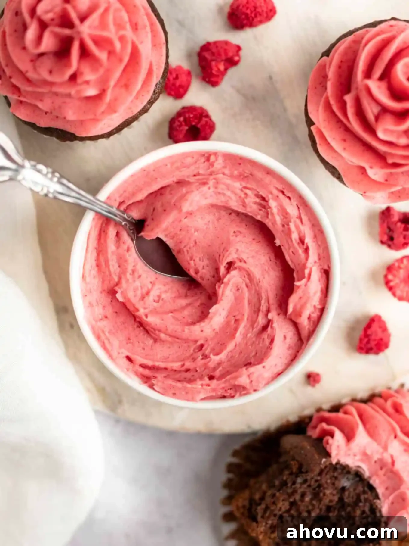 An overhead view of raspberry buttercream in a white bowl, with a spoon sticking out. 