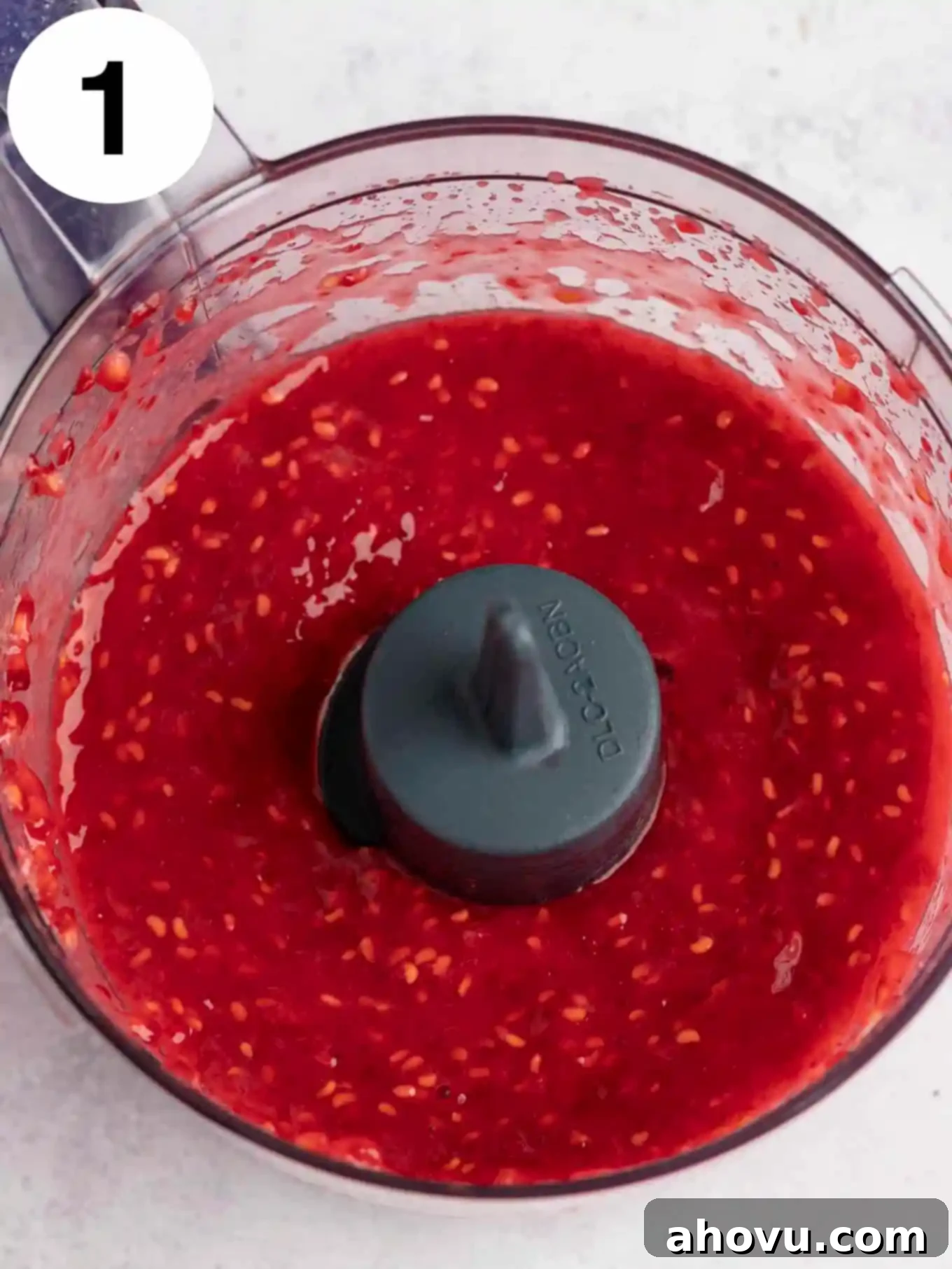 An overhead view of pureed raspberries in the bowl of a food processor. 