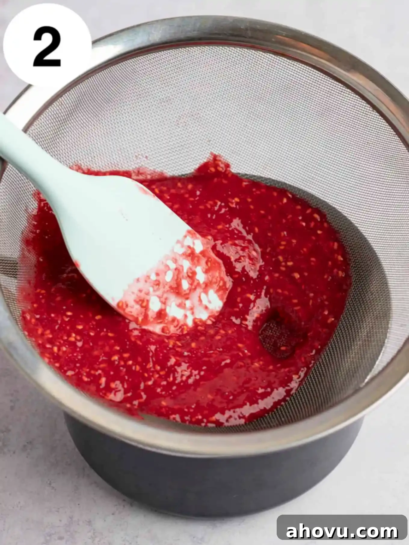 An overhead view of fresh raspberry puree being passed through a mesh sieve. 